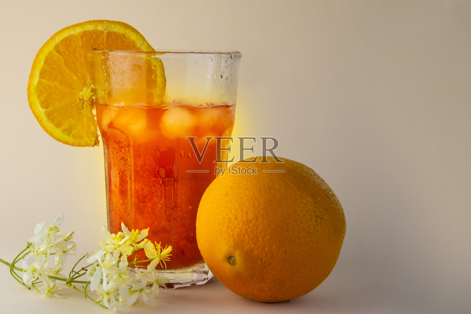 一大杯橙汁和冰块，米色背景上放着整个橙子照片摄影图片
