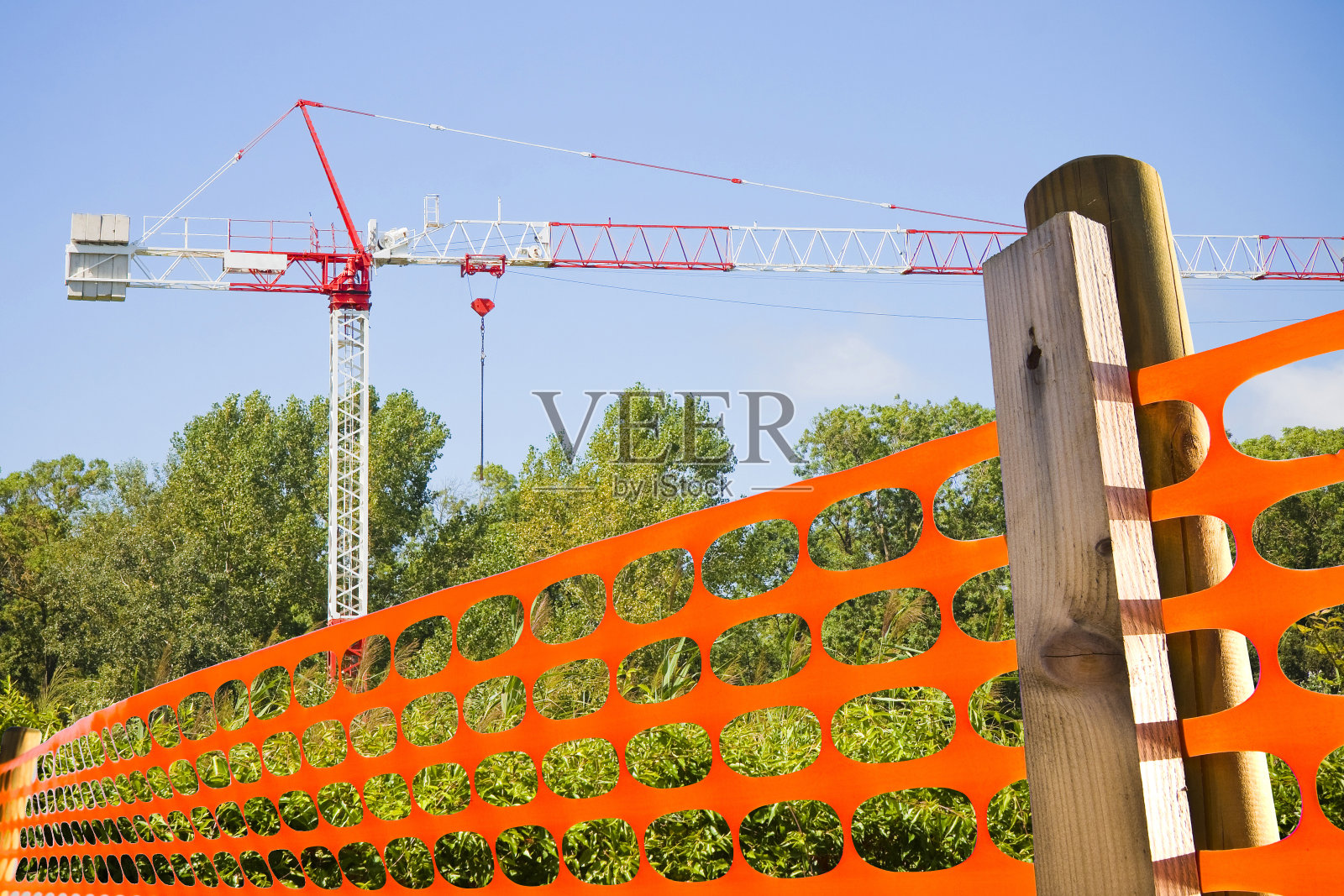 建筑工地的塔式起重机用金属脚手架在建筑立面上工作，穿孔的橙色安全塑料网格用来划定和保护建筑工地区域照片摄影图片