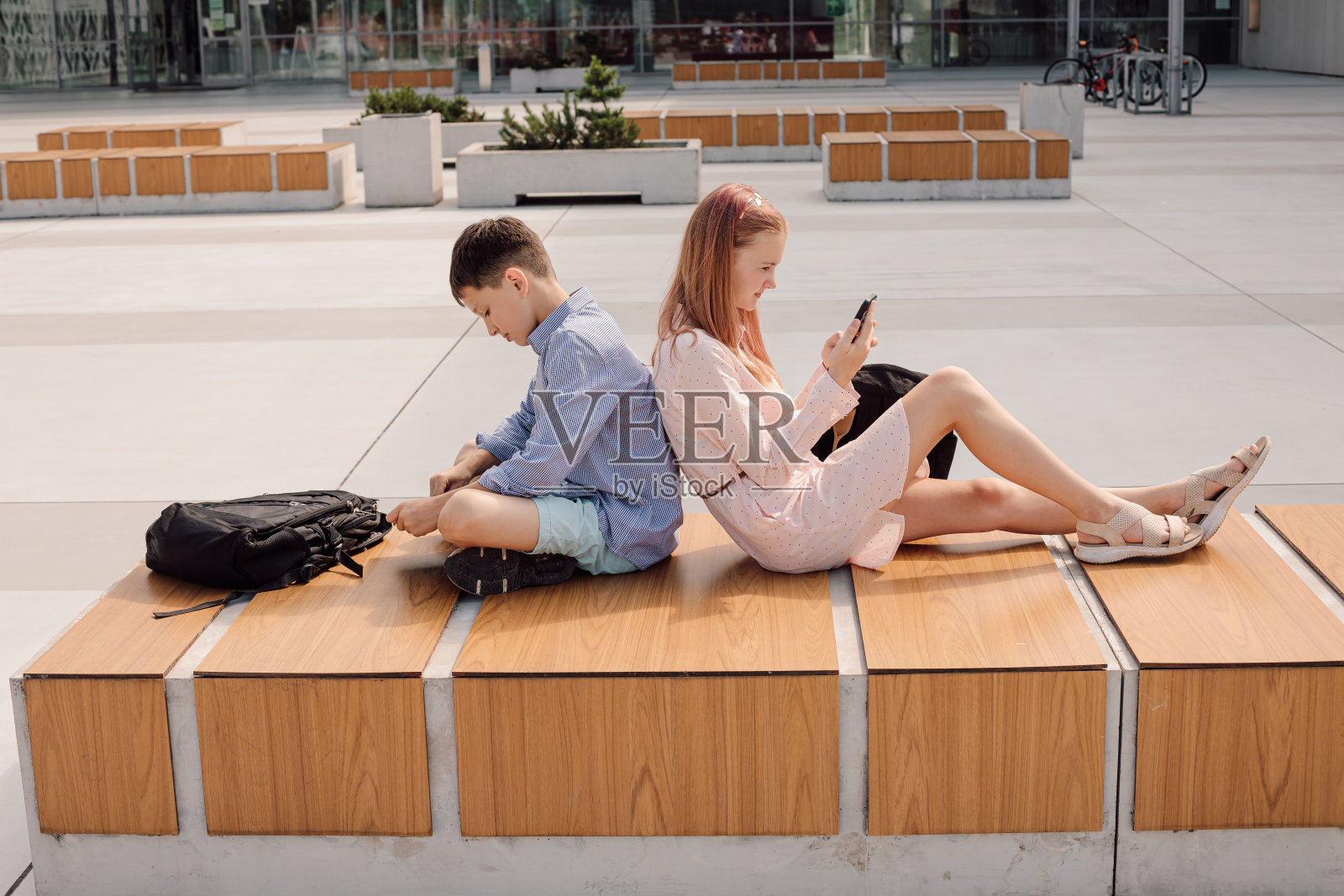 可爱的年轻学生的肖像穿着随意，背靠背坐着，手里拿着手机，认真地看着屏幕，校园附近的校园照片摄影图片