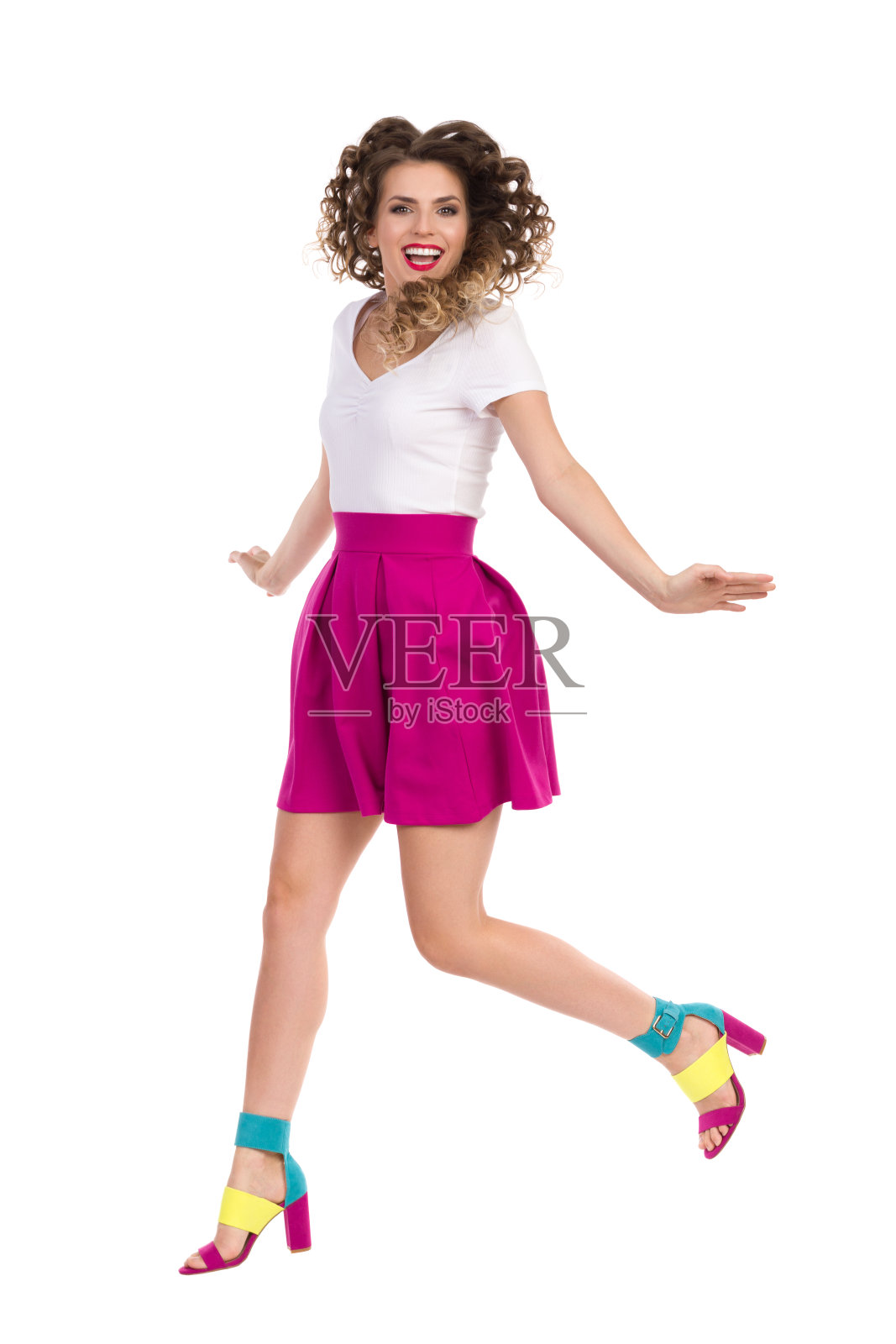 跳跃快乐的年轻女子在彩色高跟鞋和洋红迷你裙照片摄影图片