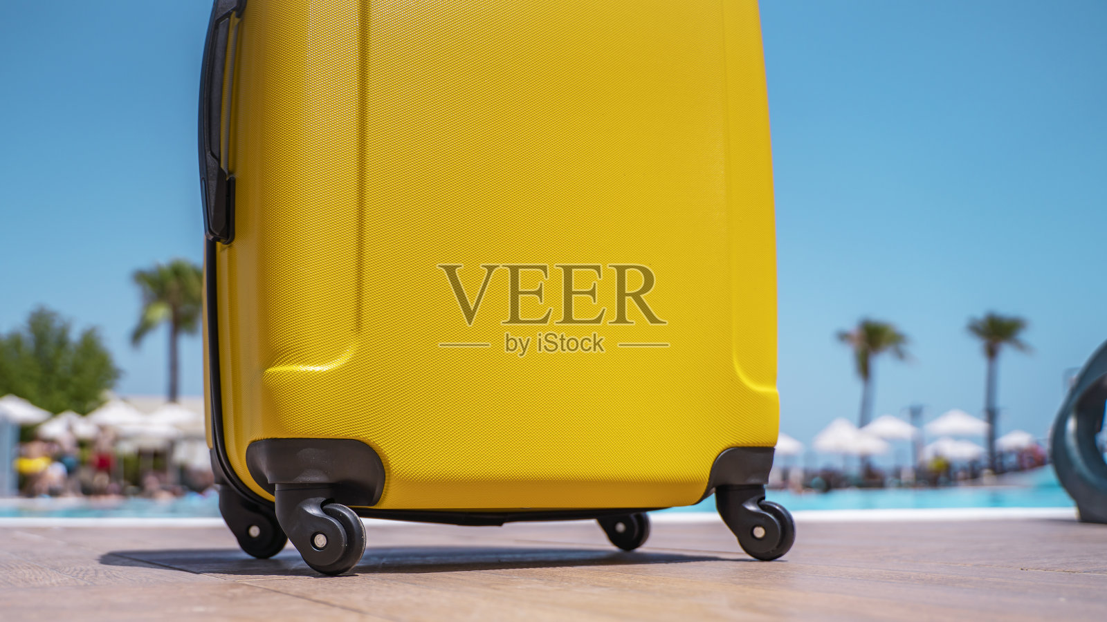 暑假的背景。在一个阳光明媚的夏日，棕榈树和蓝色无云的天空映衬着黄色带轮子的行李箱。文本复制空间照片摄影图片