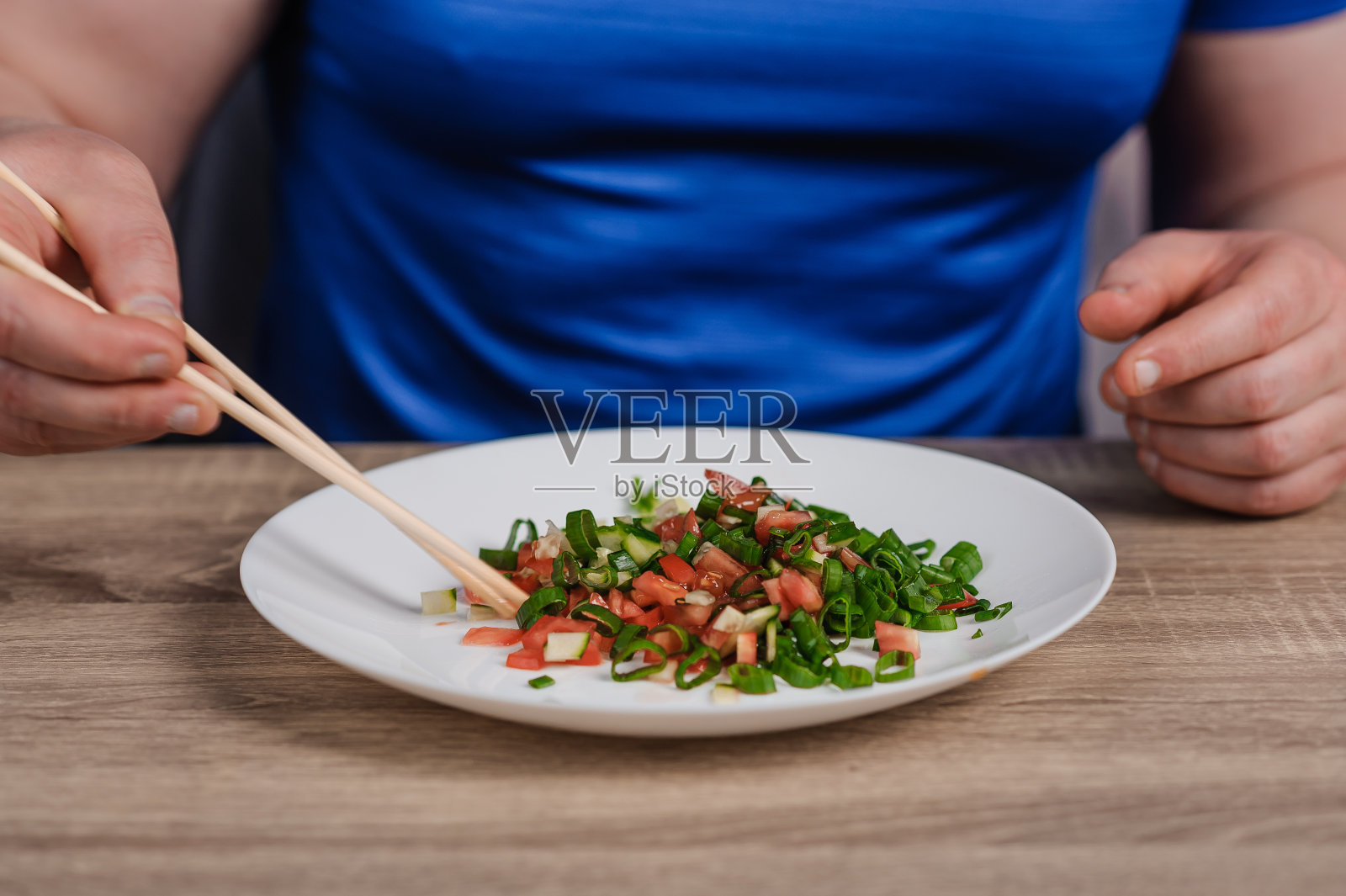 一盘有黄瓜、西红柿和大葱的沙拉。一个拿着一盘沙拉的男人照片摄影图片