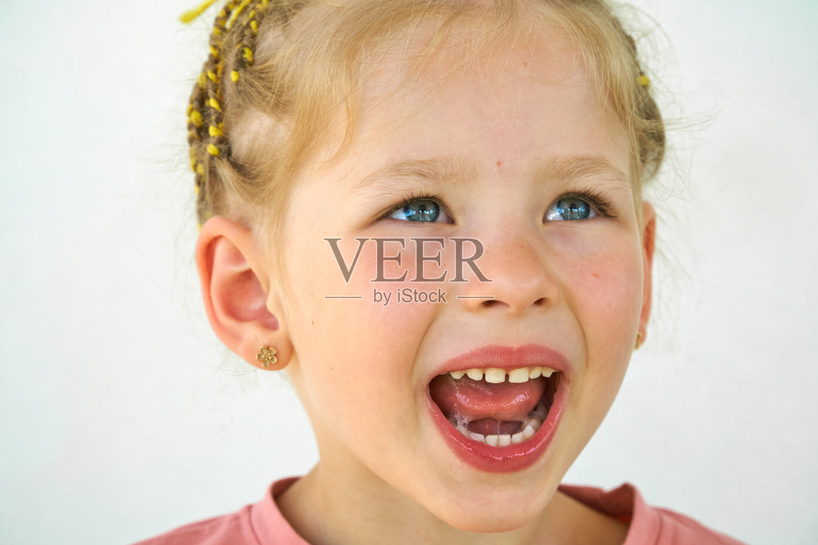 开朗的孩子。女孩笑特写的脸在白色的背景。一个小女孩露出了舌头和喉咙。张大嘴巴，伸出舌头的肖像。在视野清晰的情况下伸出长舌头照片摄影图片