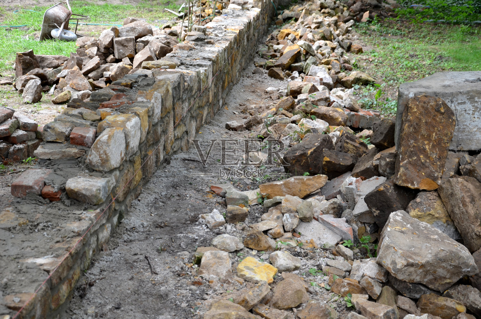 两座地块之间正在重建一堵古老的石墙。把石头拆下来，重新粘在水泥砂浆上。石匠在公园里建造了一堵墙。连接处被修复，灌木丛被保护织物覆盖照片摄影图片