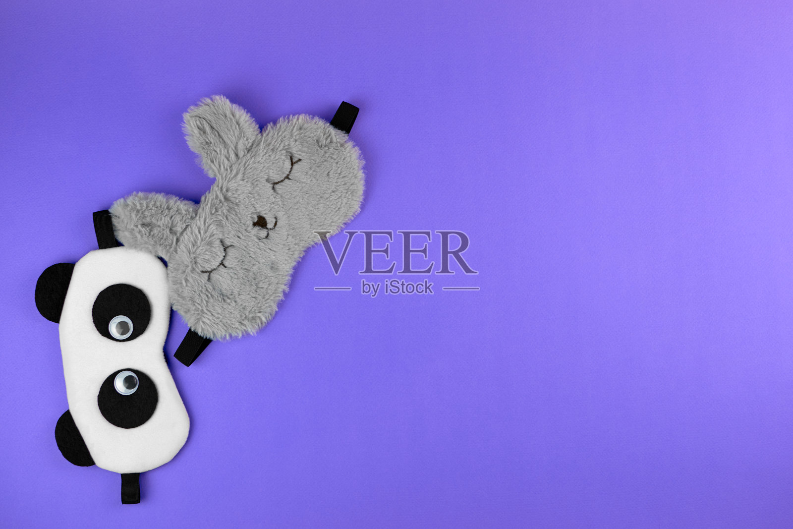 有熊猫和兔子脸的睡眠面具。可爱的紫色背景睡眠面具，俯视图。舒适睡眠的配件。照片摄影图片