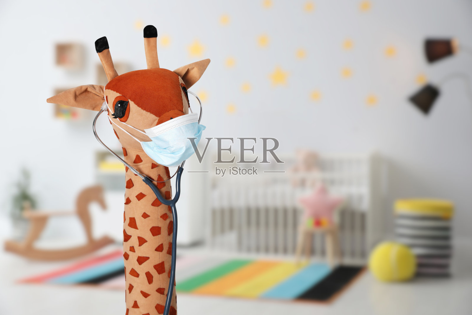 玩具长颈鹿戴口罩和听诊器室内，文字空间。儿科医生实践照片摄影图片