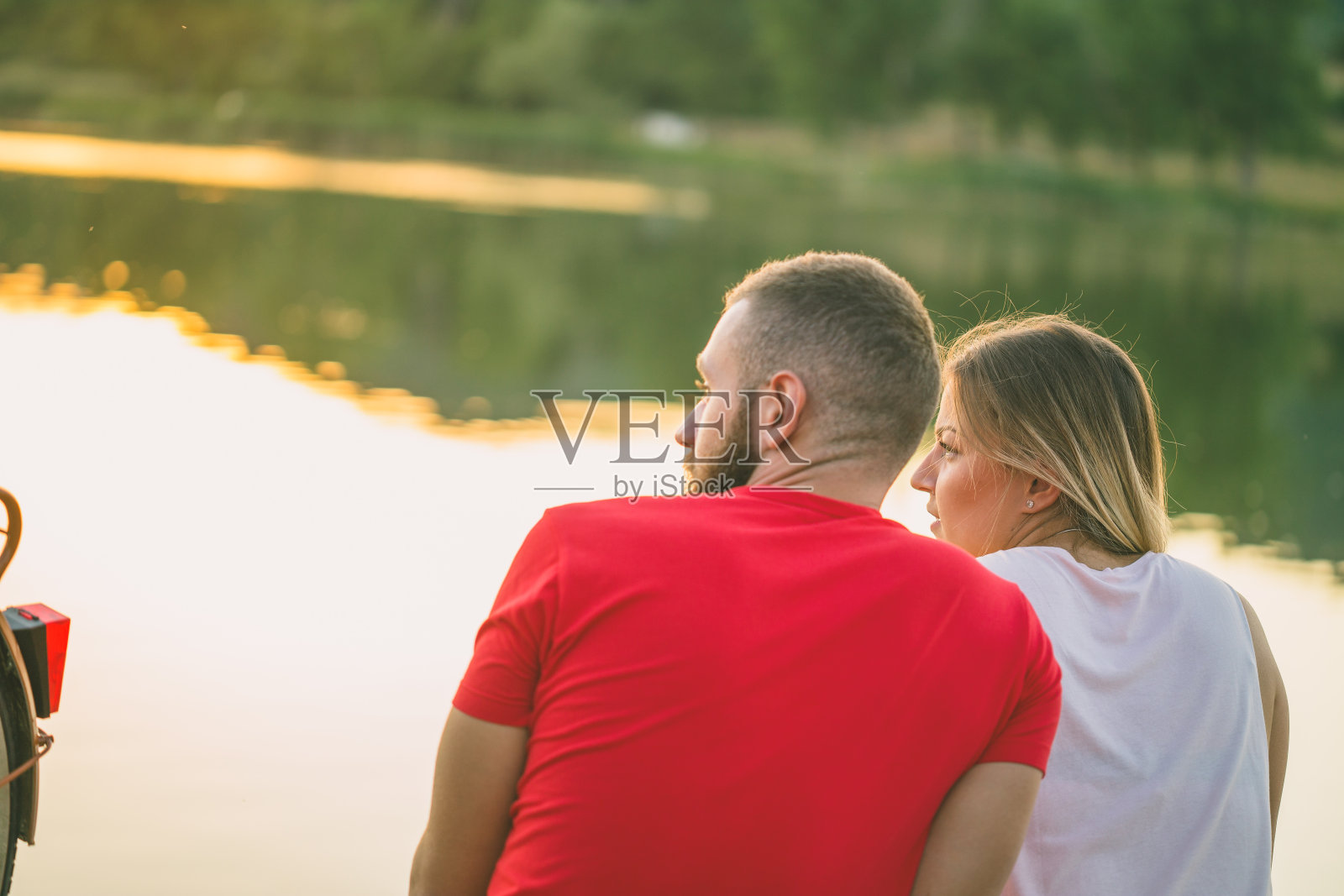 一对年轻夫妇坐在湖边码头上欣赏日落照片摄影图片
