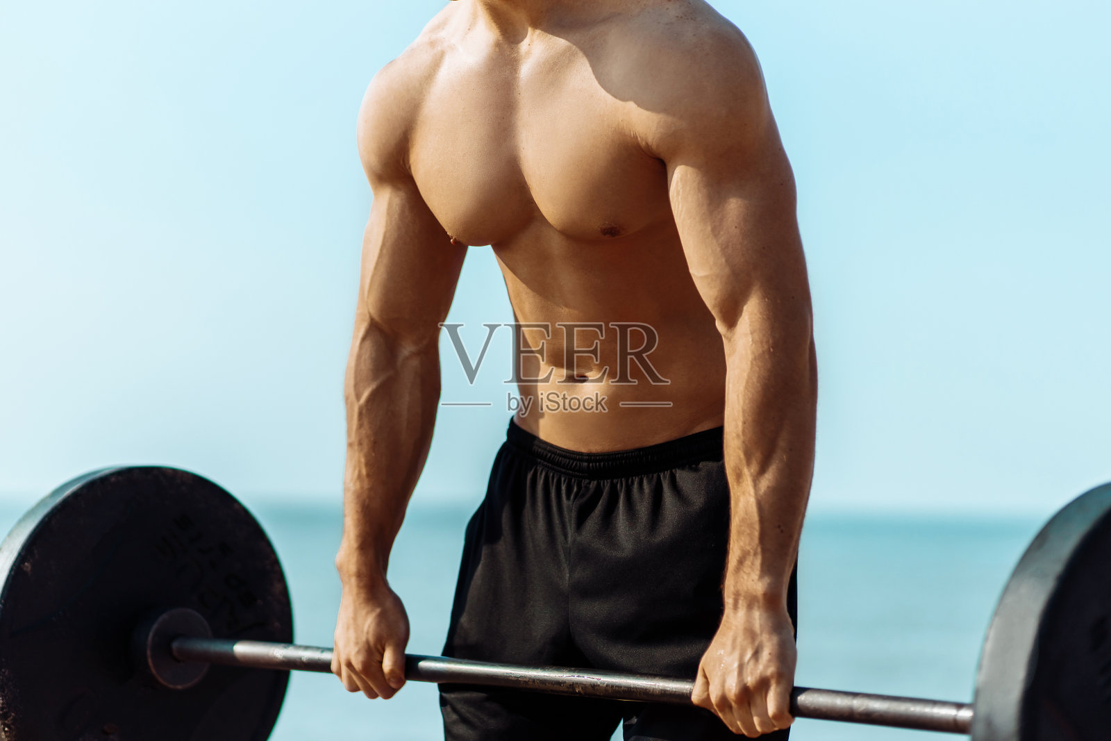 年轻的肌肉男用哑铃做胸部锻炼，在沙滩上，一个肌肉发达的男人照片摄影图片