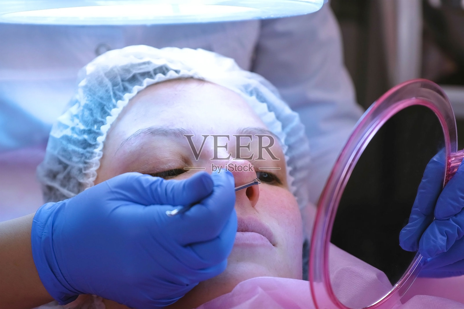 在美容师那里机械清洁脸部。美容师在镜子前给病人看她脸上的东西。脸特写。照片摄影图片