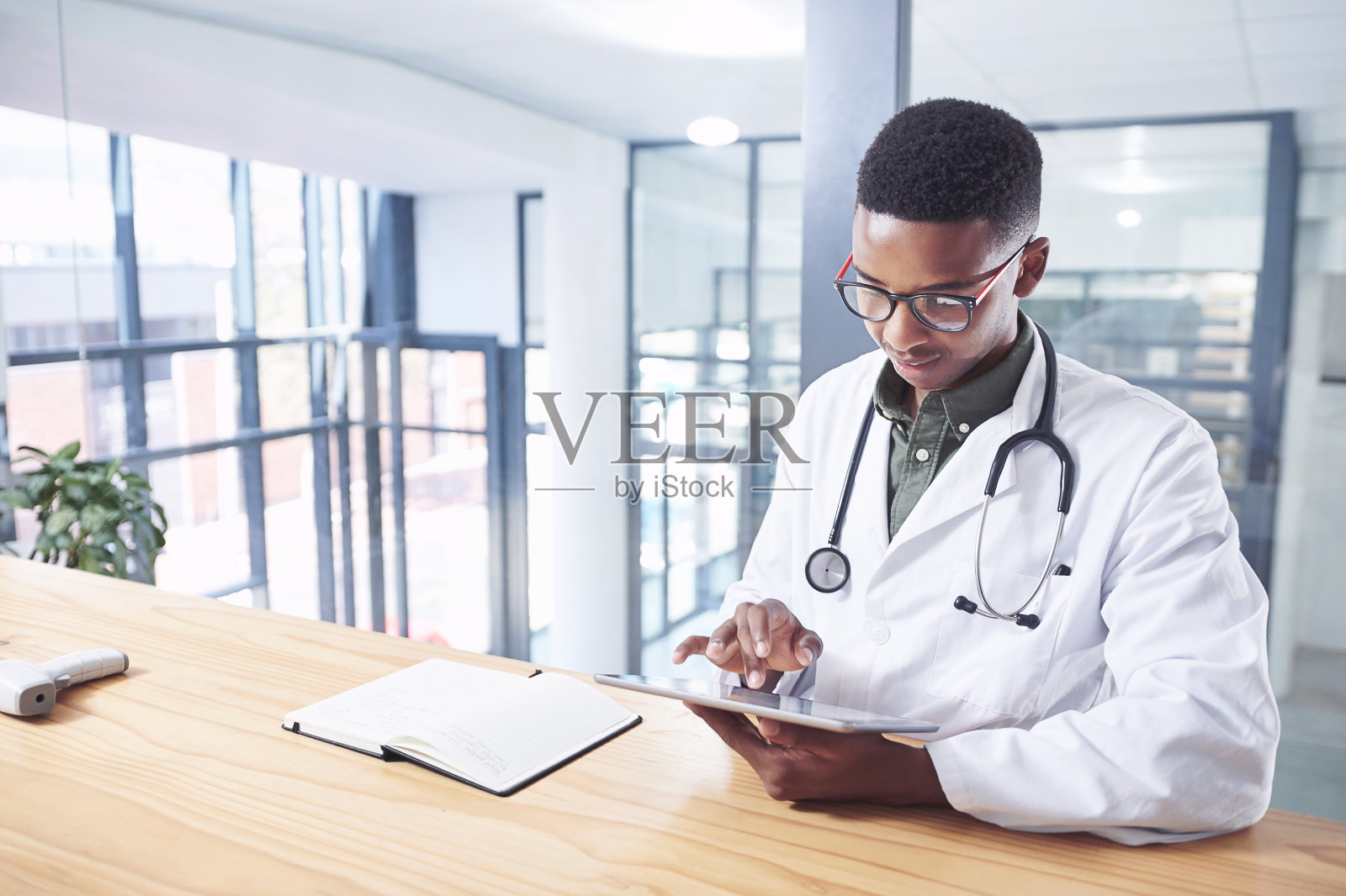 一个英俊的年轻医生独自坐在诊所的办公室里使用他的电子平板电脑照片摄影图片