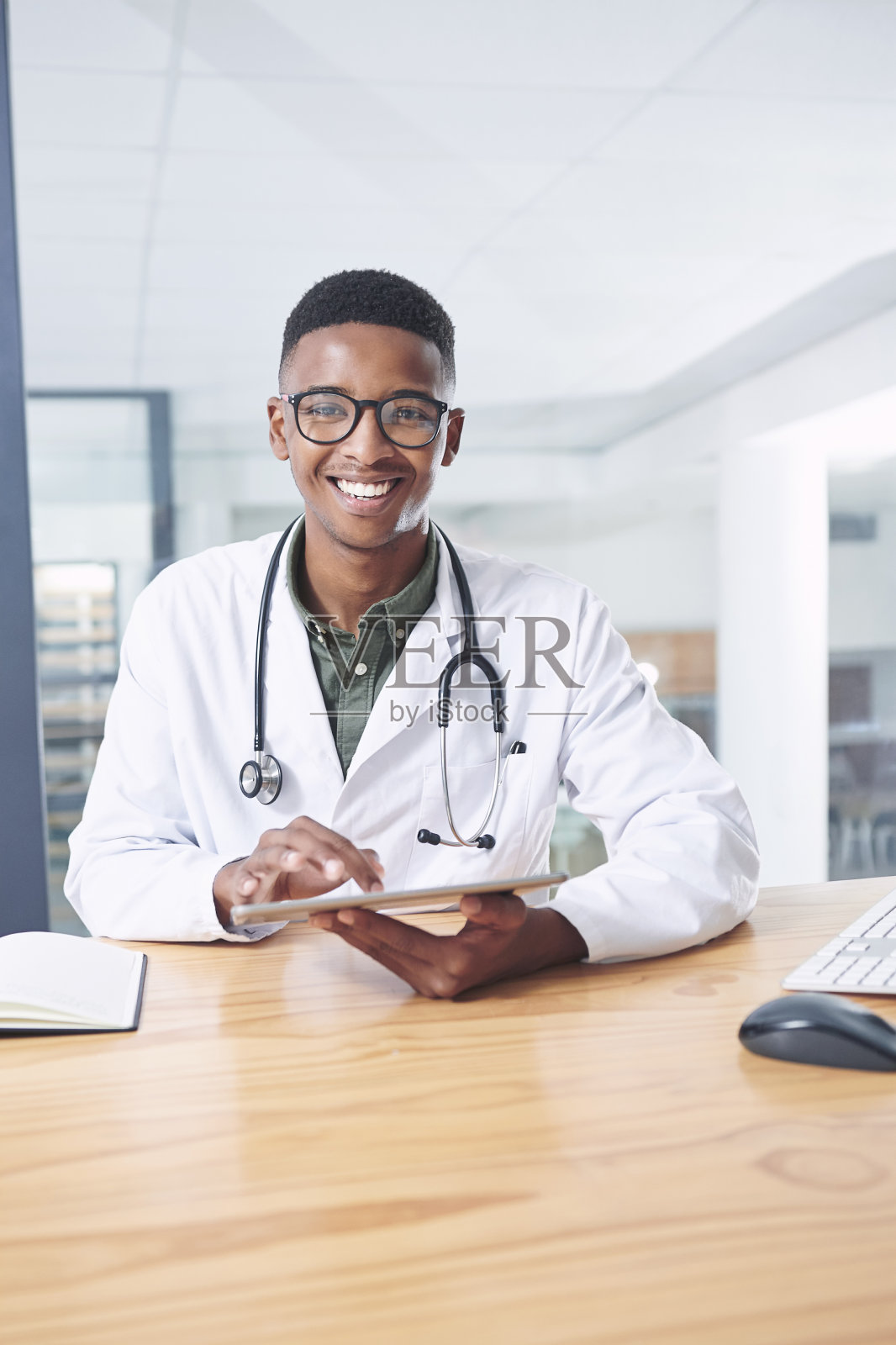 一个英俊的年轻医生独自坐在诊所的办公室里使用他的电子平板电脑照片摄影图片