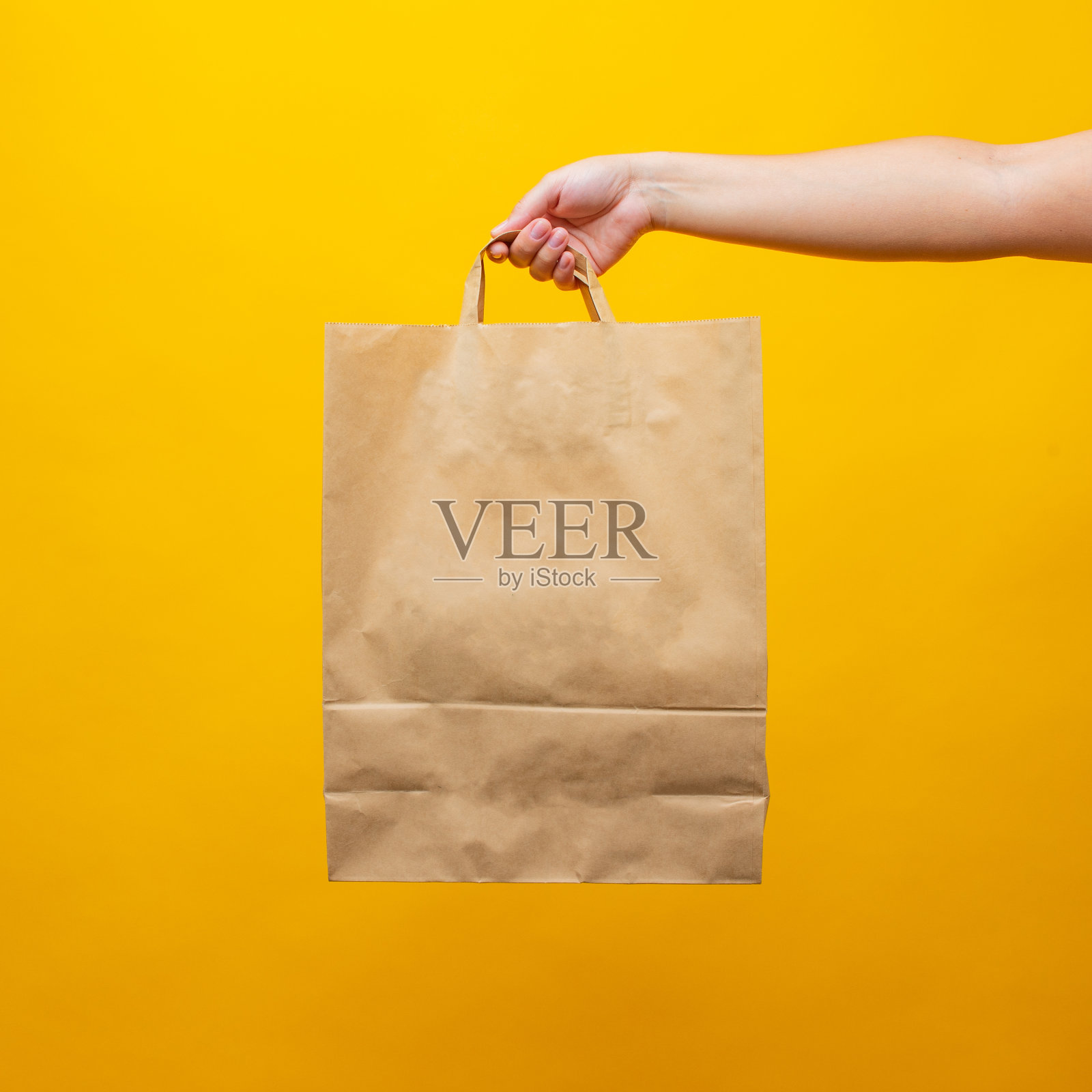 一个女人的手，黄色背景上有一个纸袋照片摄影图片