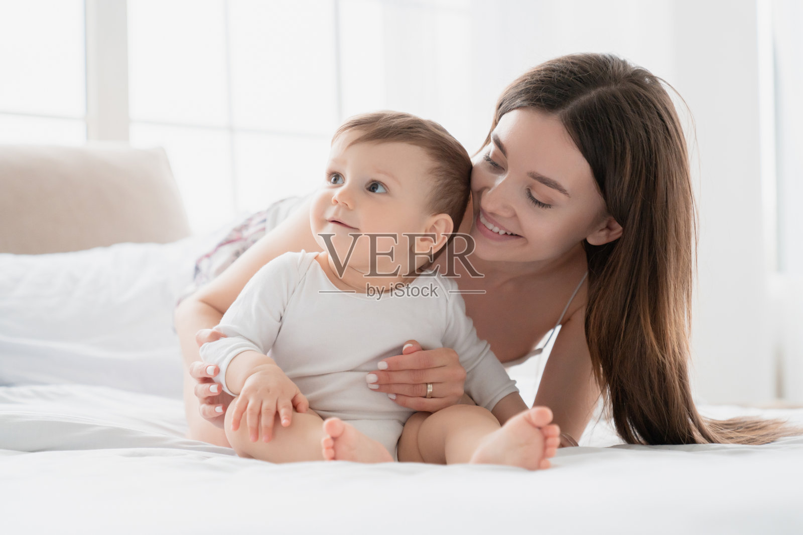 家庭时间。快乐的年轻单身母亲和儿子女儿婴儿，新生儿婴儿，蹒跚学步的孩子一起在床上玩耍。母亲节快乐!产假和母性照片摄影图片