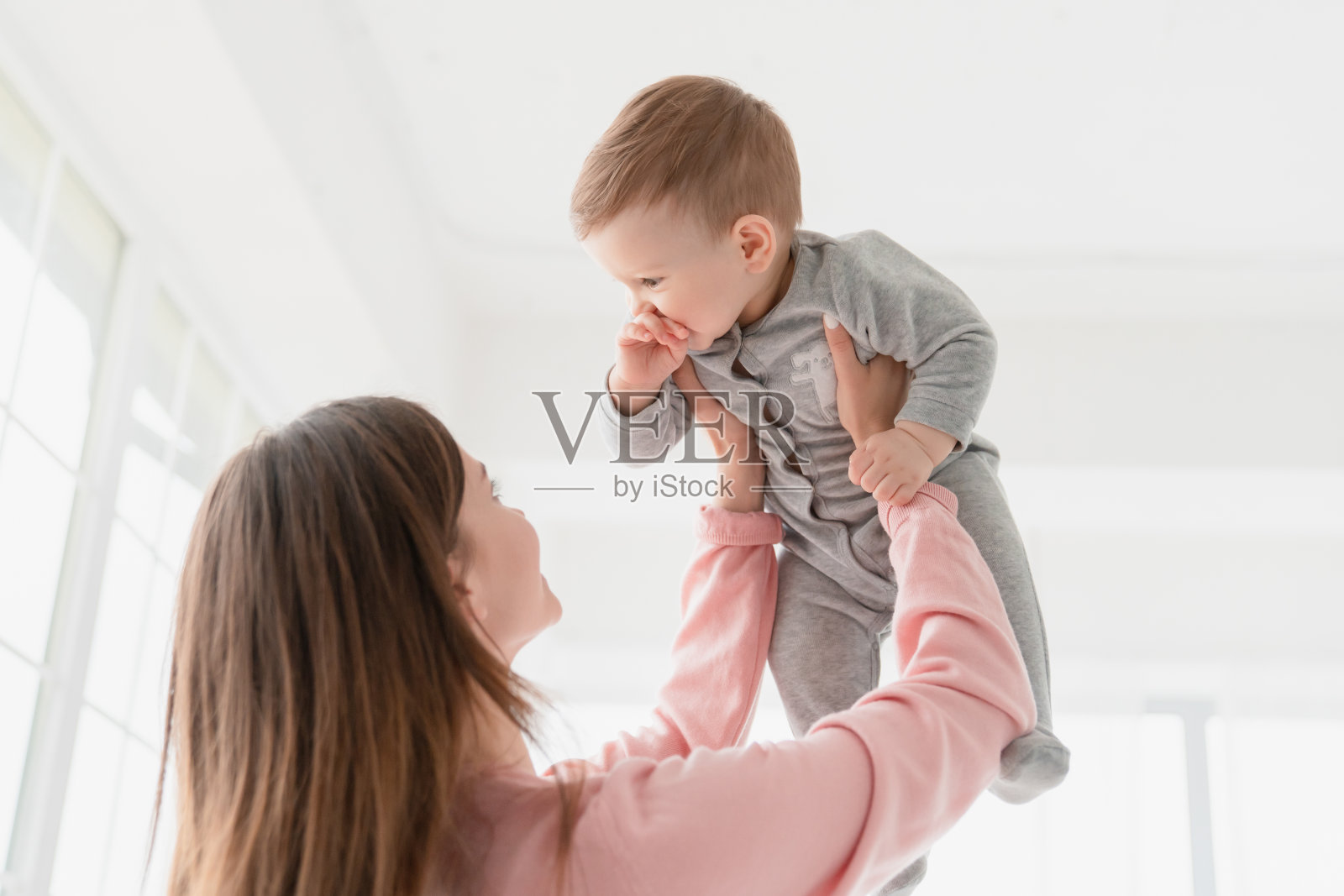 快乐的年轻妈妈抱着她的小宝贝和刚出生的小宝贝玩耍，给他爱和照顾。母亲和儿童保育，收养概念照片摄影图片