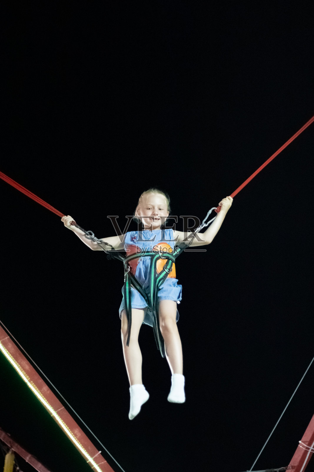 金发小女孩坐在弹弓上，在黑色的天空中飞翔。有趣的暑假照片摄影图片