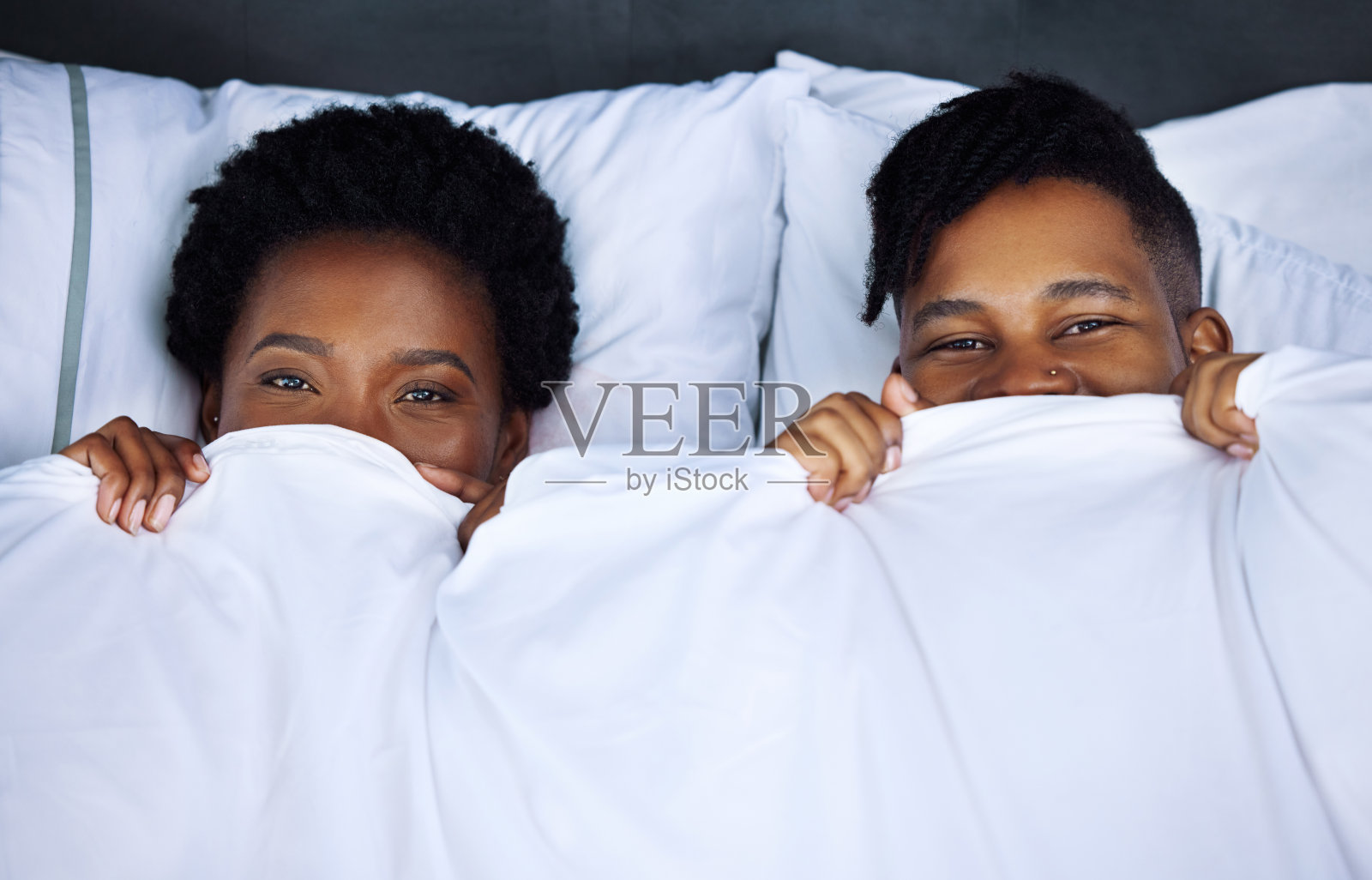 一对年轻夫妇躲在家里的床上照片摄影图片