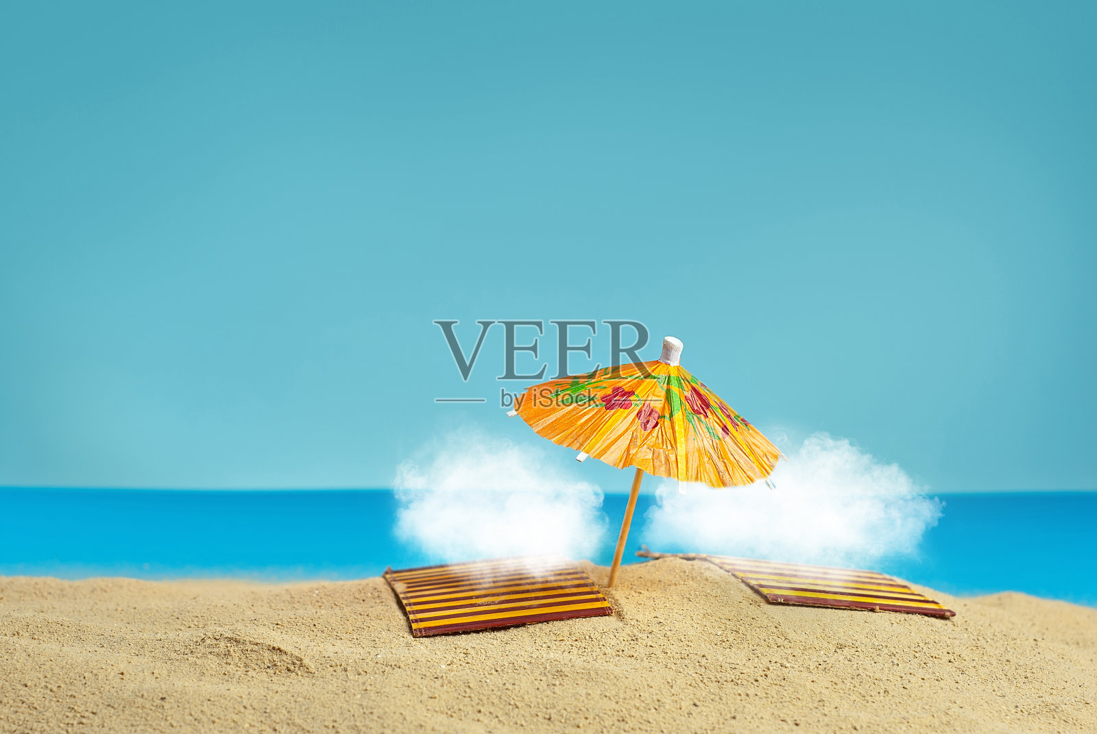 沙滩伞和沙滩上的日光浴床。程式化的纸板海滩。背景是用来装鸡尾酒的纸伞。白云在沙滩上晒日光浴。照片摄影图片