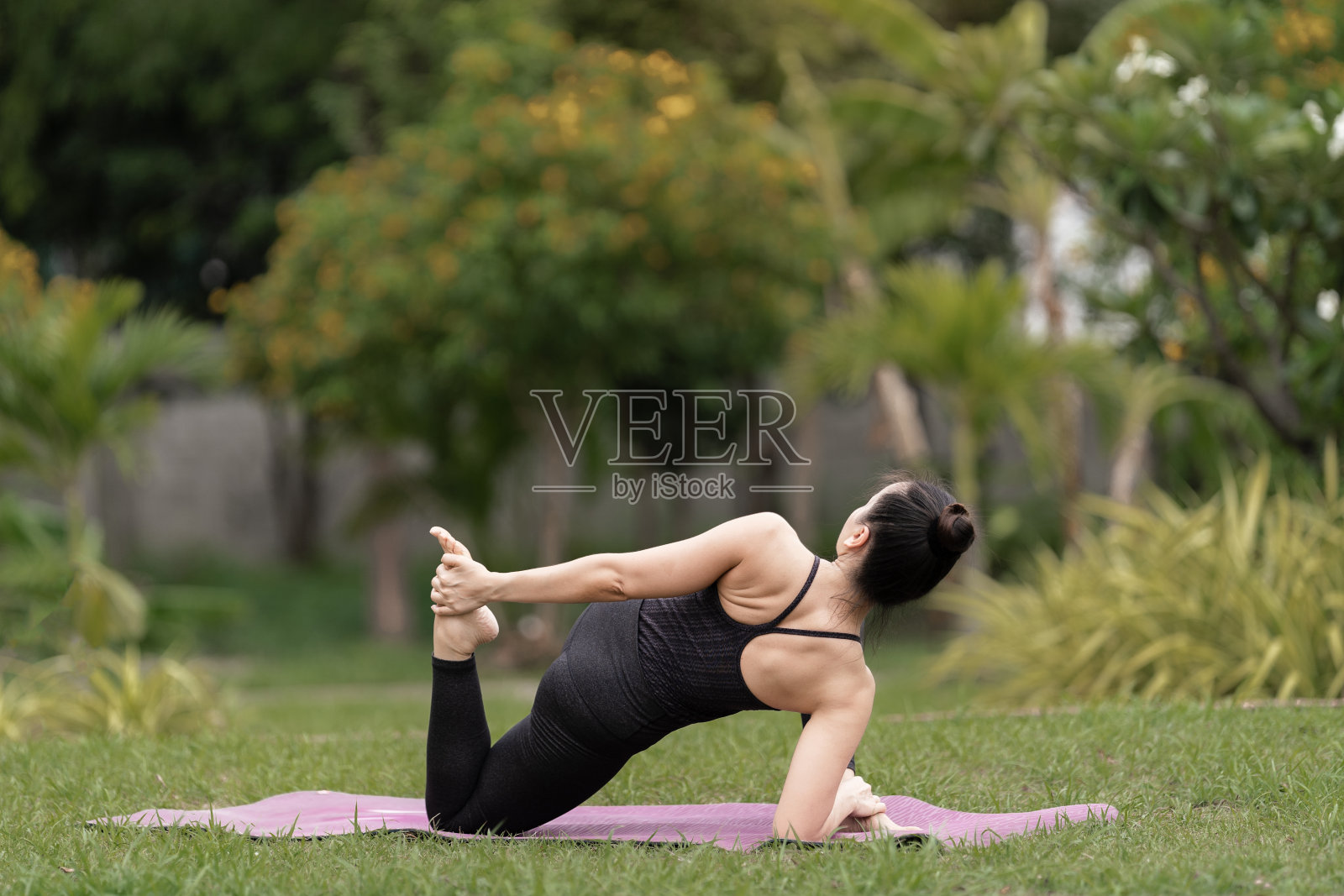 一个自信的亚洲中年妇女，穿着运动服，在后院的瑜伽垫上做瑜伽练习。年轻女子在户外做瑜伽运动的自然公园照片摄影图片