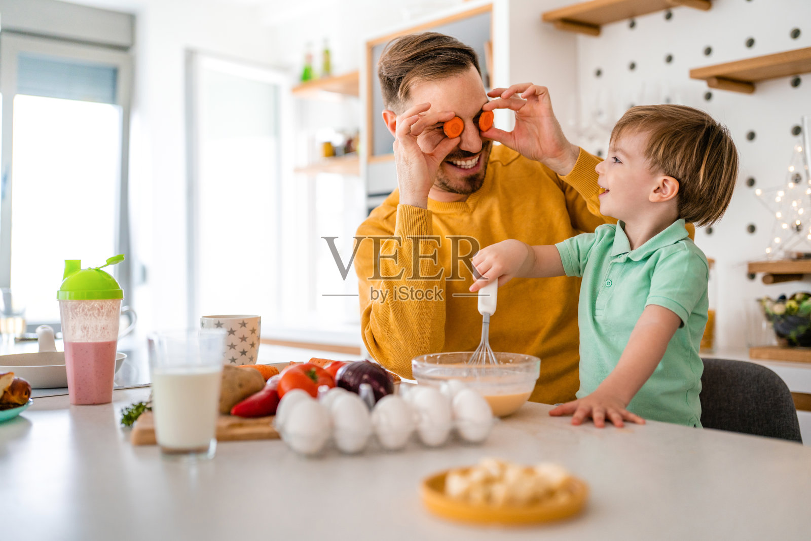 快乐的单身父亲和一个蹒跚学步的男孩在家里的厨房里准备健康的食物。照片摄影图片