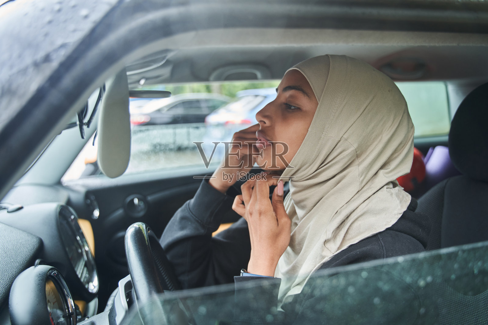 一位女士一边坐着一边对着汽车后视镜纠正她头上的围巾照片摄影图片