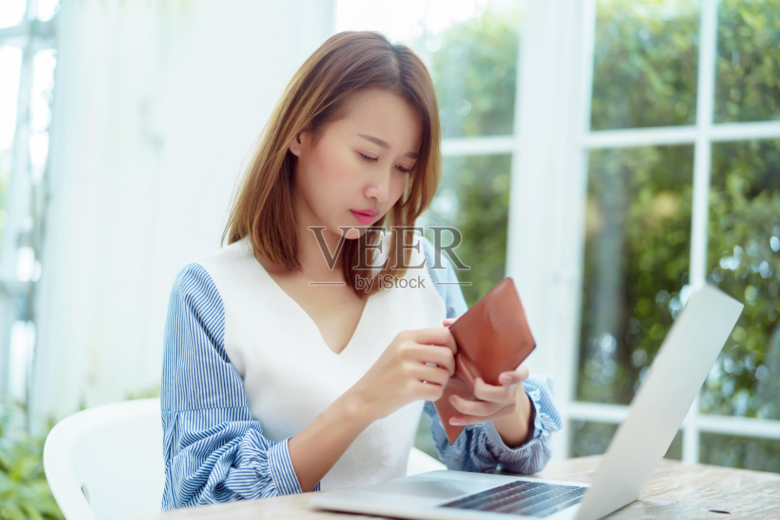 一个穿着白衬衫的亚洲女人的半身像坐在面包店里检查她的钱包里的钱，一脸的紧张和不高兴。照片摄影图片