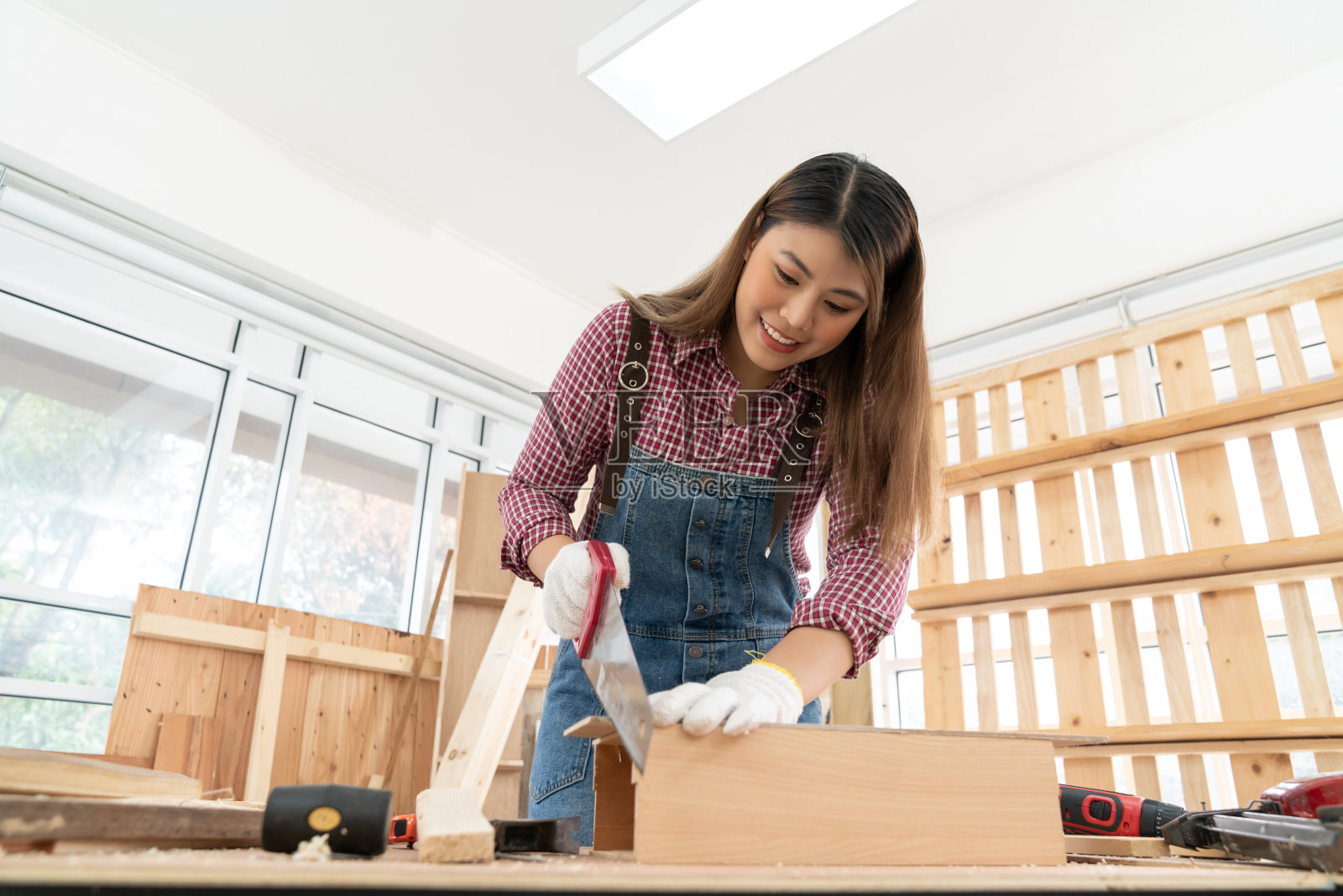 自信的年轻女木匠正在木工店用手锯锯木头照片摄影图片