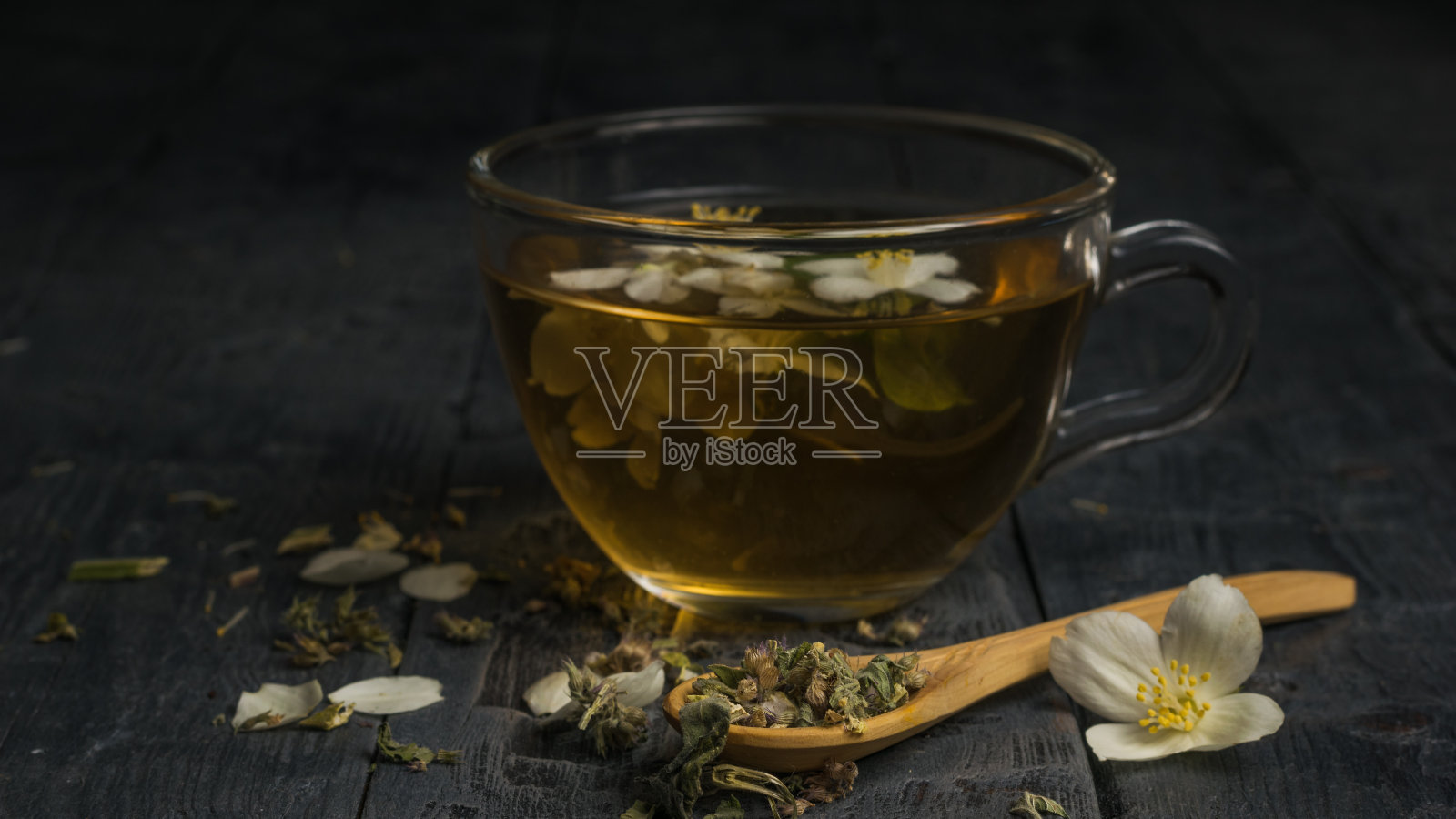 在黑色的桌子上，有一个玻璃杯和一个木勺，里面放着花茶。照片摄影图片