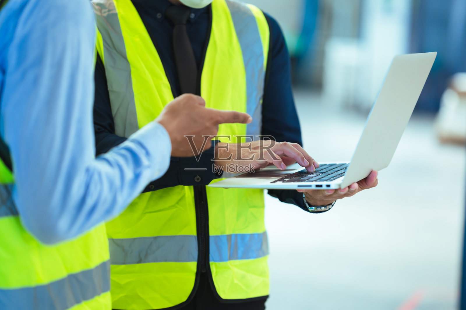 总工业工程师视察口罩厂。使用笔记本电脑时讨论新项目。他们表现出坚定的态度。有穿着防护服的员工在勤奋地工作。照片摄影图片