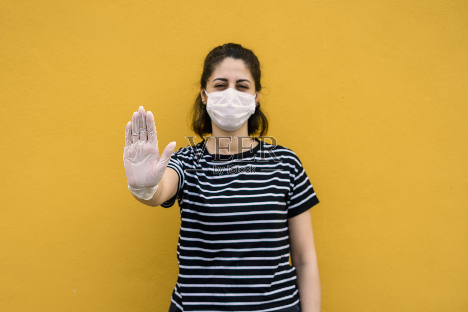 漂亮的女人在手套和面罩显示停止标志的黄色背景照片摄影图片