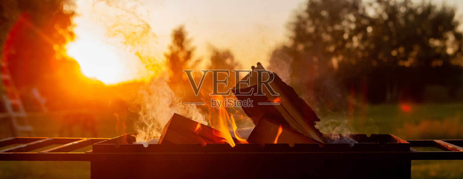 火在烤架上燃烧，有木柴和烟。在日落的自然背景上。露营的概念。照片摄影图片