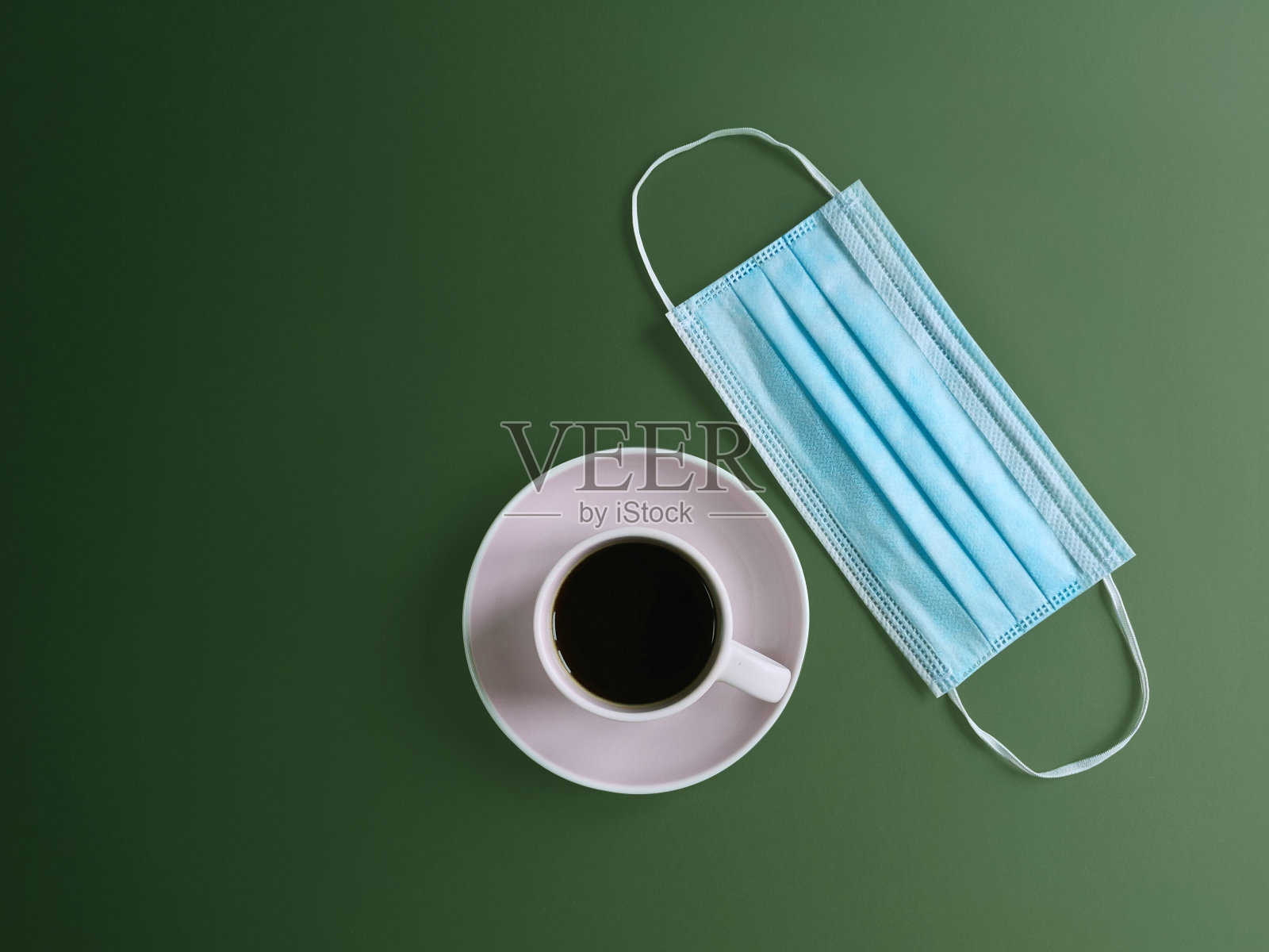 外科耳罩和一杯绿色背景的咖啡。医用口罩可以预防冠状病毒或隔离COVID-19。生命的生物学概念在一个新的现实。平躺照片摄影图片