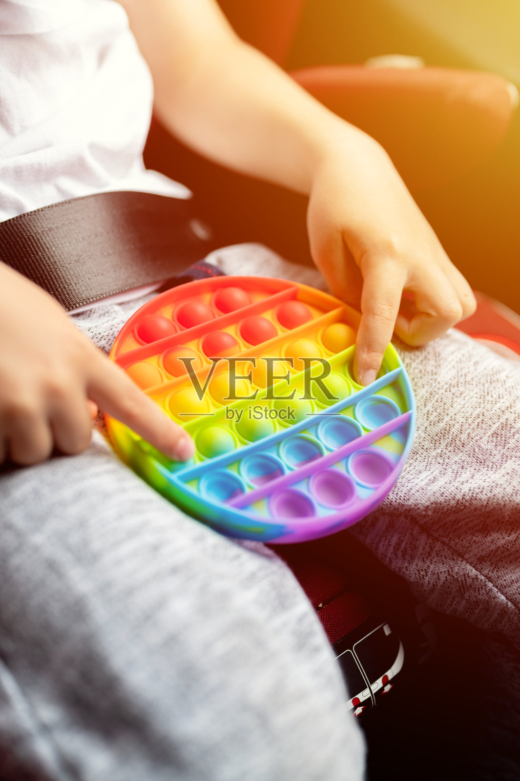 抗压力感应器把玩具放在孩子手中。一个快乐的小男孩在车里玩一个简单的酒窝玩具。幼儿抱着玩popit彩虹色相亮色，2021年流行照片摄影图片