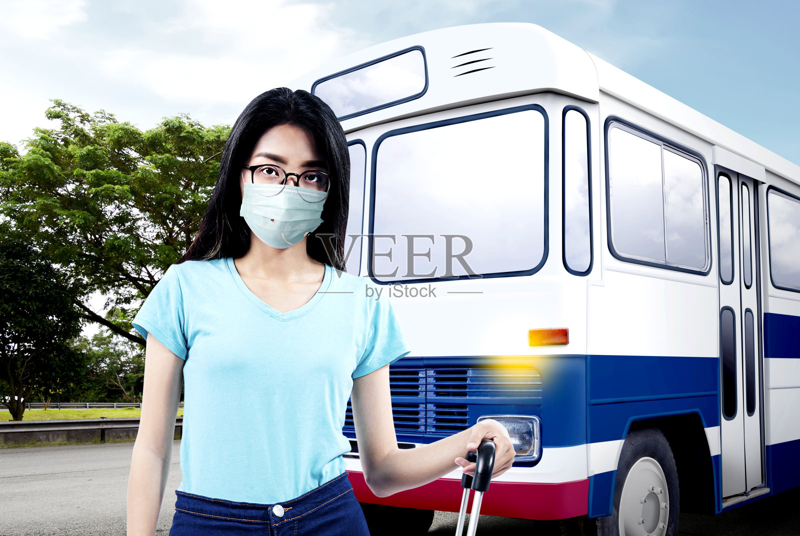 一名亚洲女子戴着口罩和眼镜，拿着行李箱站在巴士终点站照片摄影图片