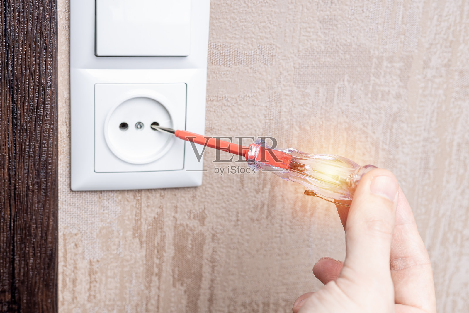 在公寓里修理墙壁插座的杂工。工人使用电压测试仪检查插座。电工服务理念照片摄影图片