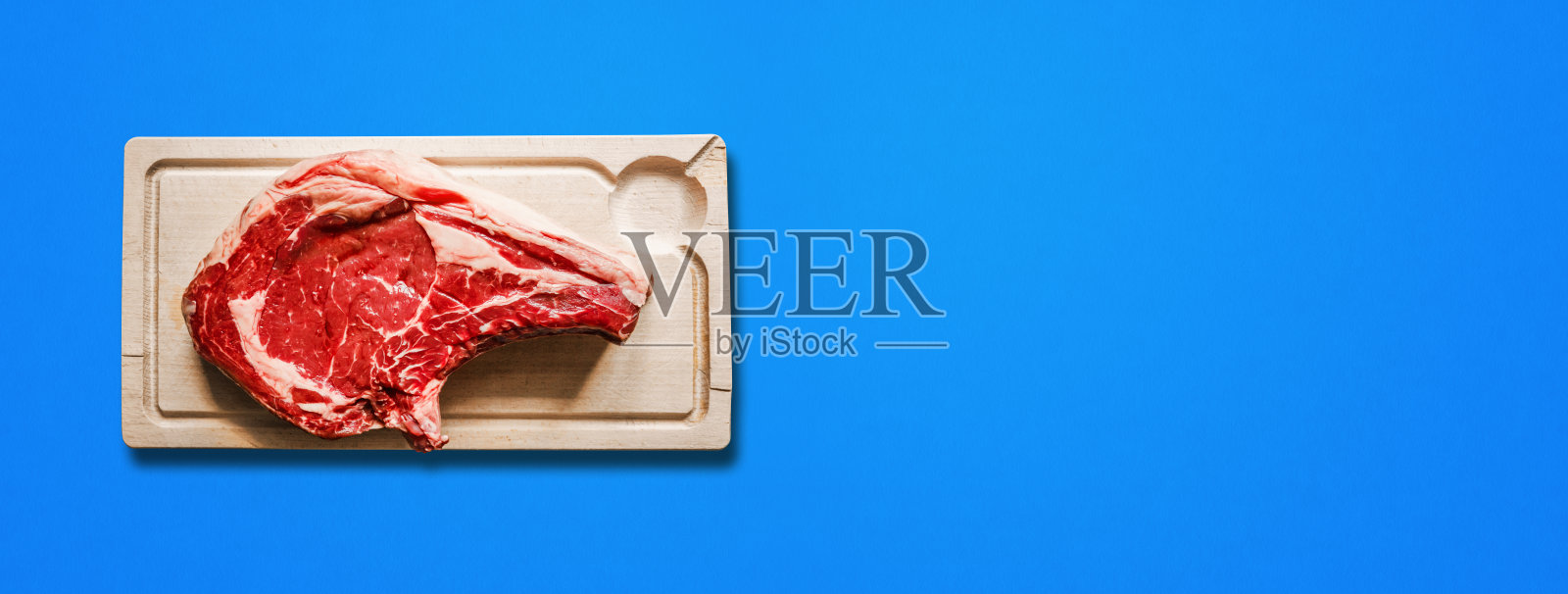 牛肉上等肋排和木制砧板孤立在蓝色。水平的旗帜照片摄影图片