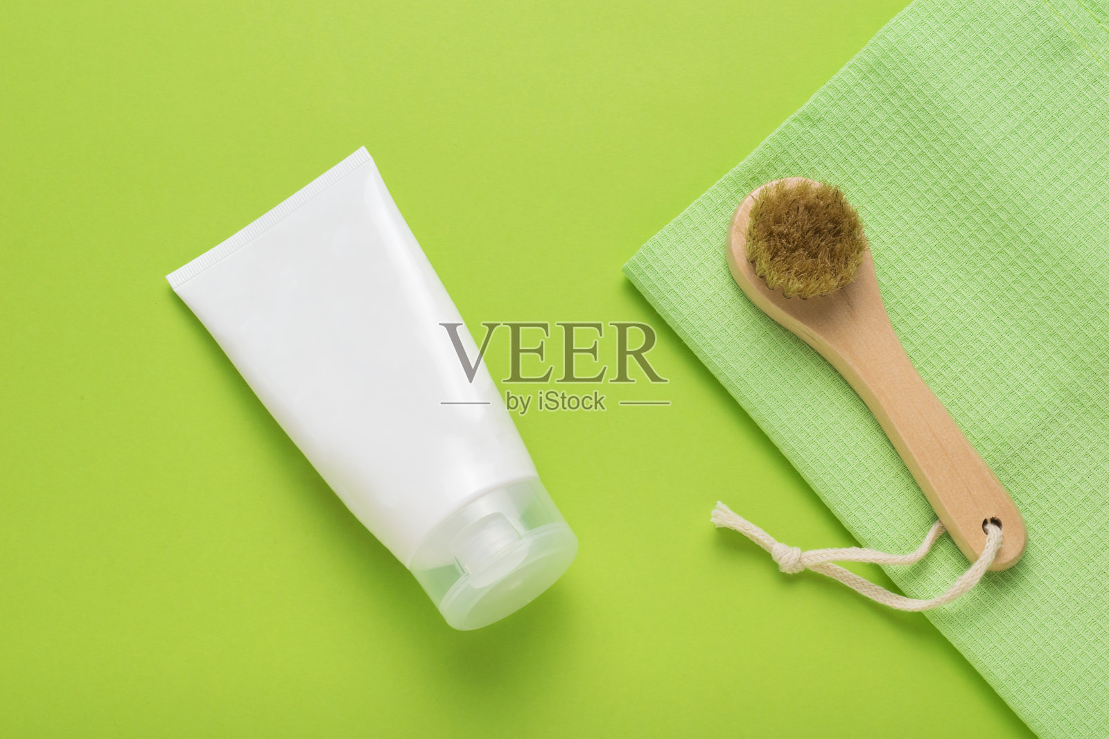 绿色背景上有一管白色的奶油和一个面部按摩器。水疗中心。平的。照片摄影图片