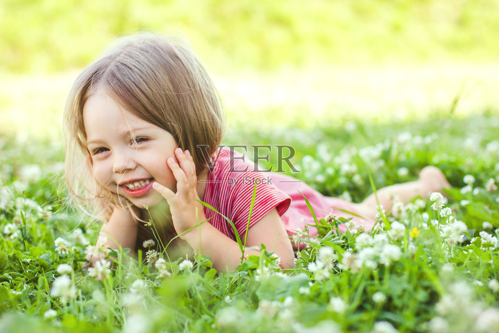 一个穿着浅色衣服的快乐的小女孩正躺在公园的绿草地上。温柔聚焦母亲节，对家庭的爱，对父亲的爱，对童年的观念照片摄影图片