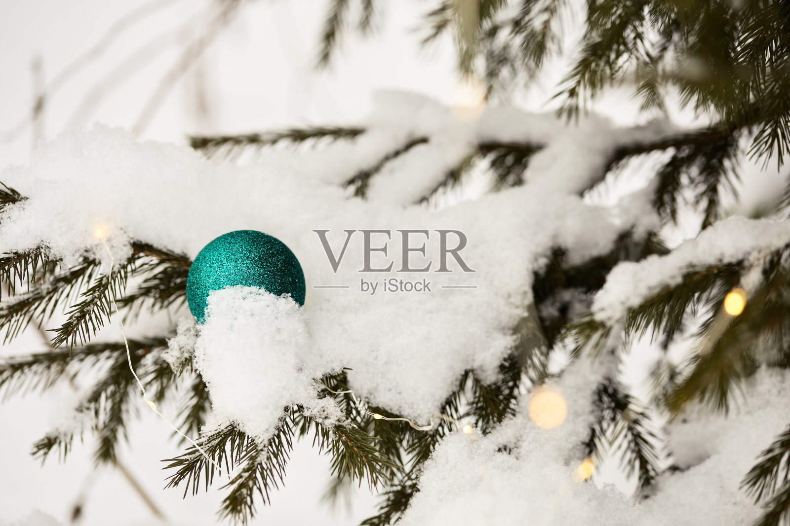 圣诞节的背景。在白雪覆盖的圣诞树树枝上装饰着美丽的绿色圣诞装饰，还有一个美丽的黄灯花环照片摄影图片