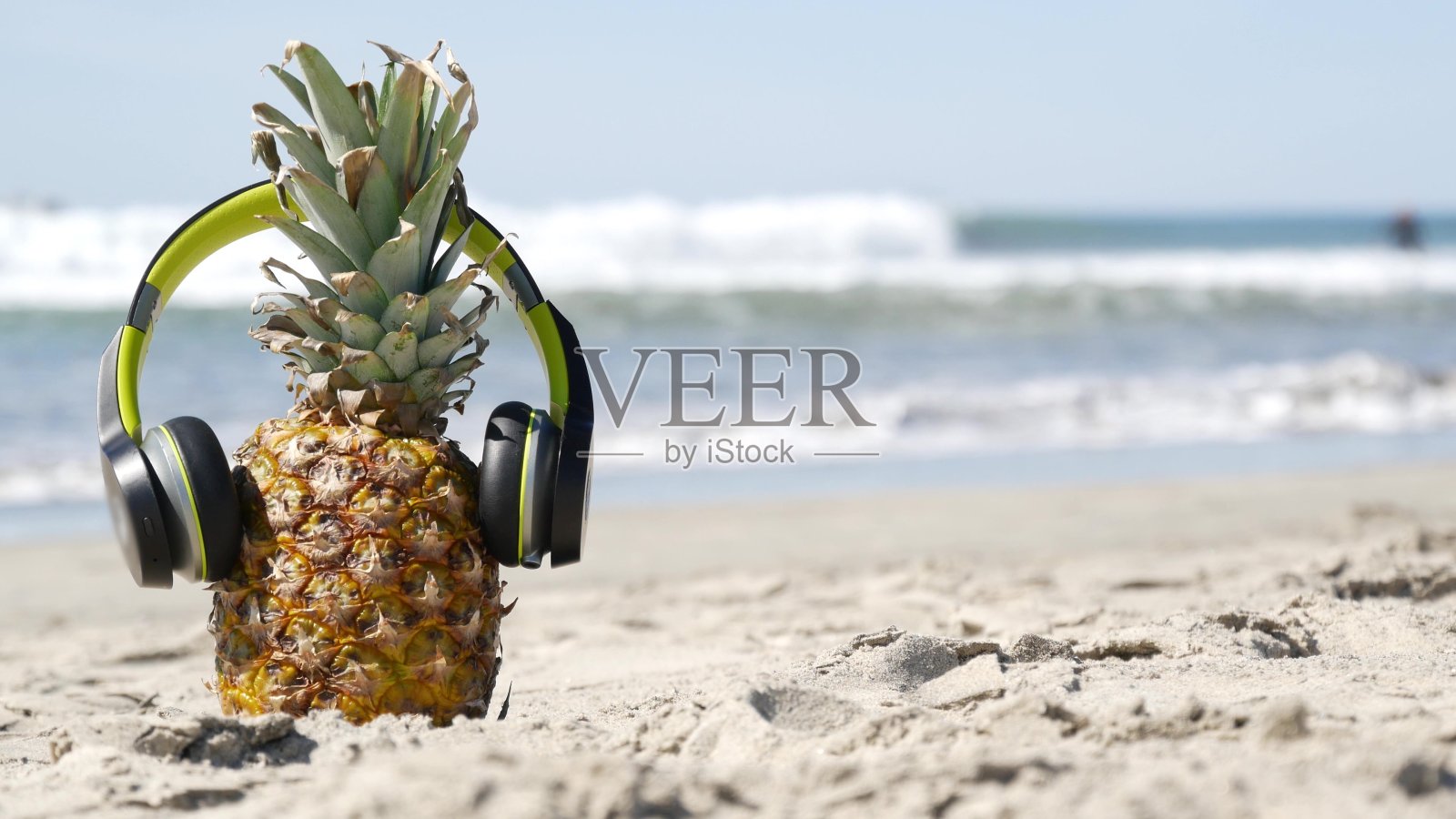 戴着耳机的菠萝，沙滩沙滩海岸。热带夏季外来水果。菠萝在岸上。照片摄影图片