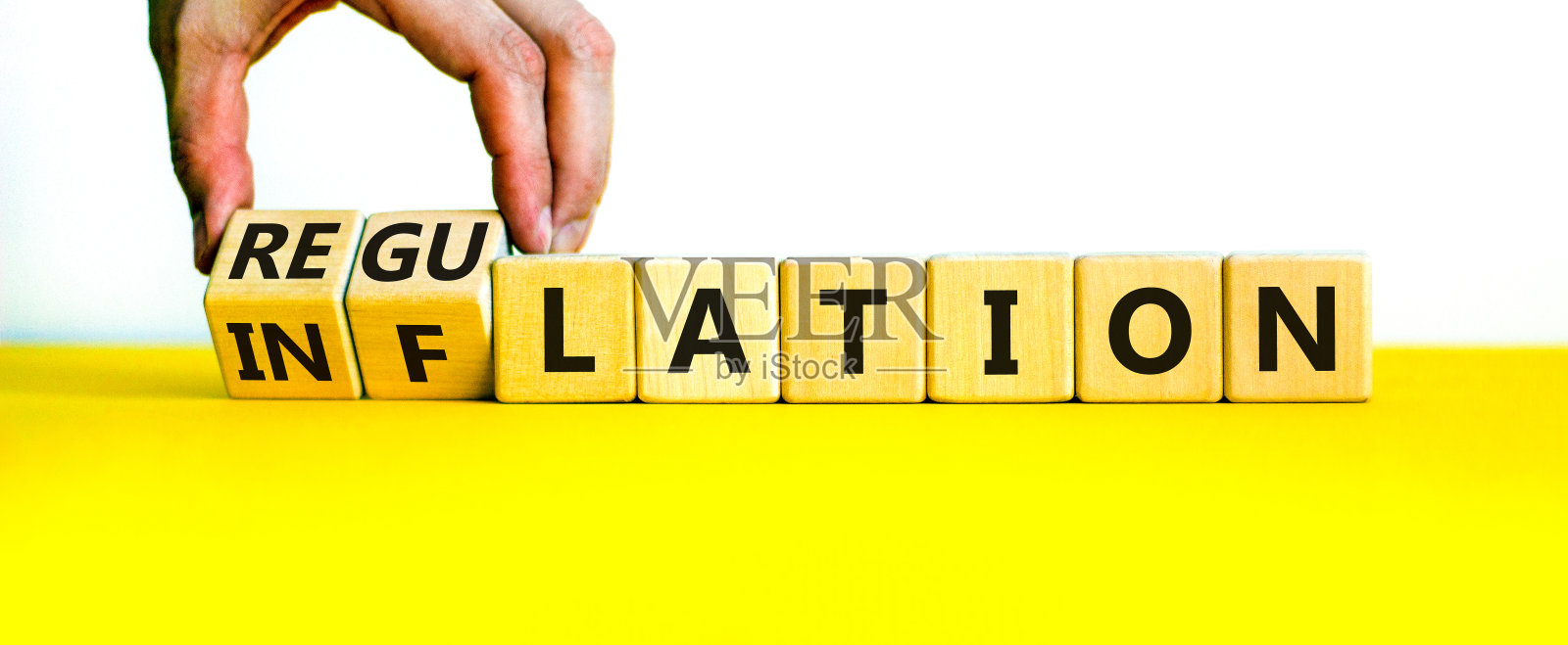 通货膨胀或监管符号。商人翻了个方块，把通货膨胀这个词变成了管制。漂亮的黄色桌子，白色背景，复制空间。商业、通货膨胀或监管概念。照片摄影图片