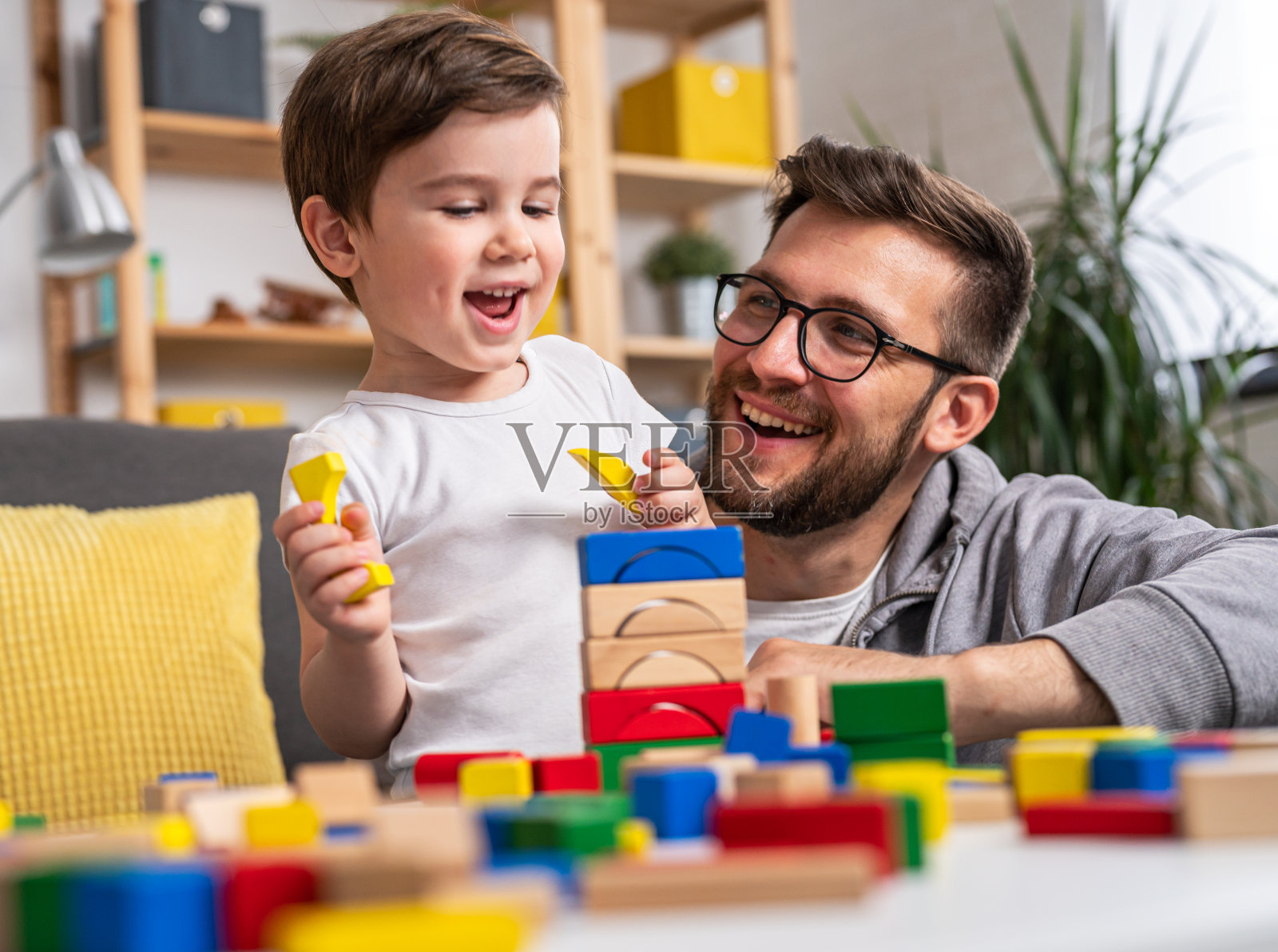 年轻的幸福的家庭。妈妈和爸爸在家里和她可爱的蹒跚学步的儿子玩木制玩具。家庭教育照片摄影图片