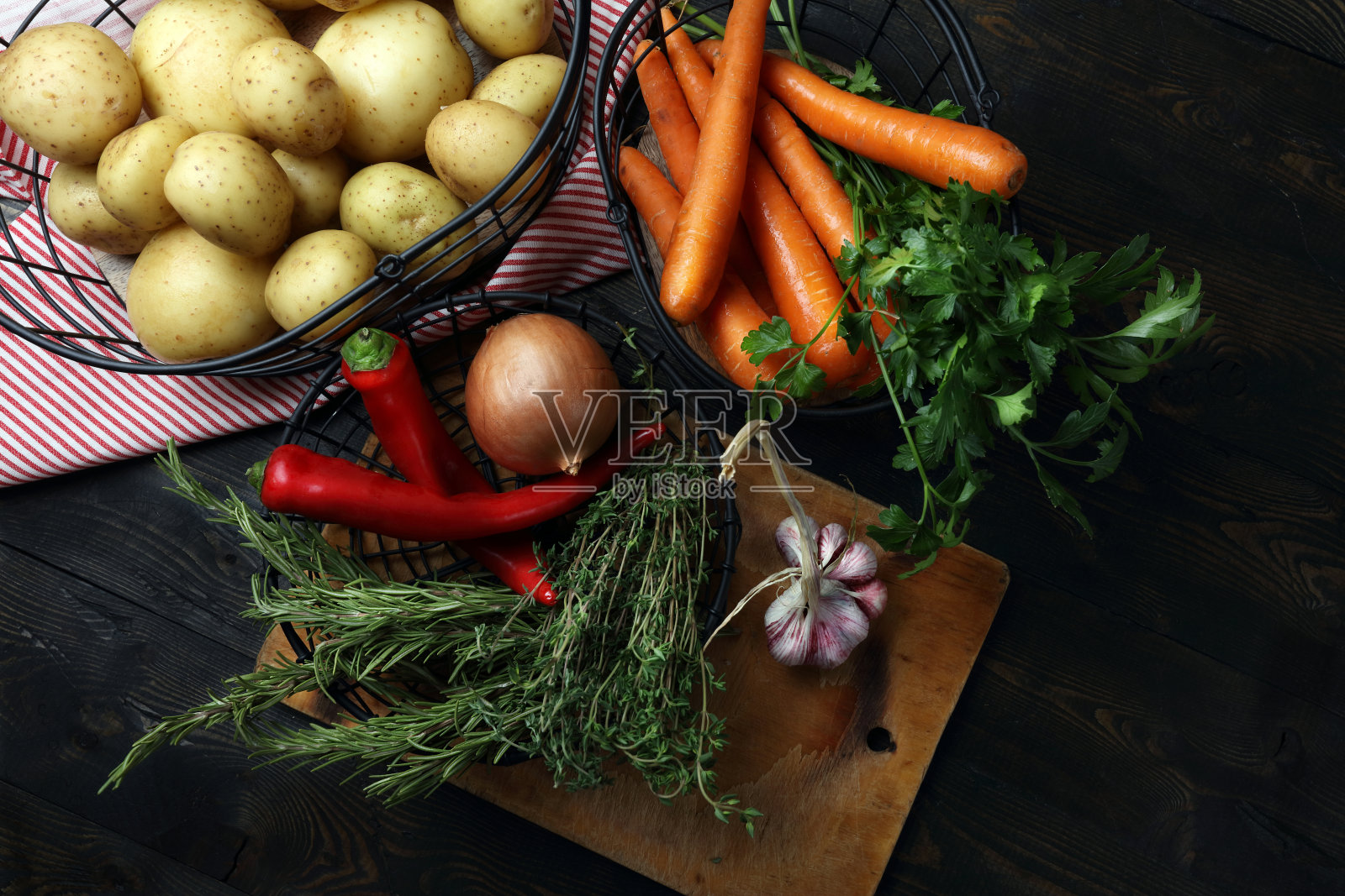 生土豆、胡萝卜、洋葱、大蒜、辣椒、百里香、迷迭香和欧芹装在金属篮子里放在桌子上照片摄影图片