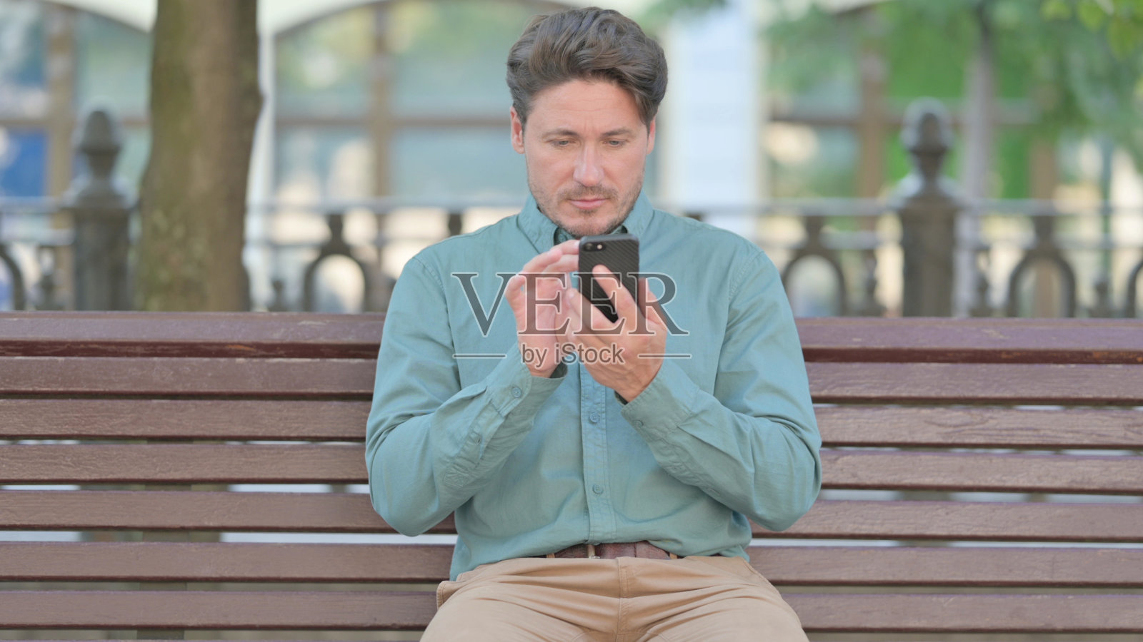 中年男子在户外用智能手机浏览照片摄影图片