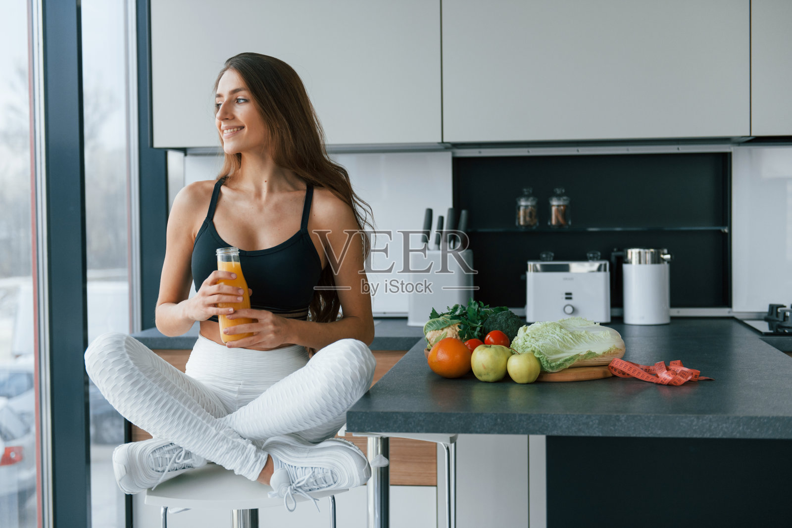 加鲜橙汁。年轻的欧洲妇女在厨房里吃着健康的食物照片摄影图片