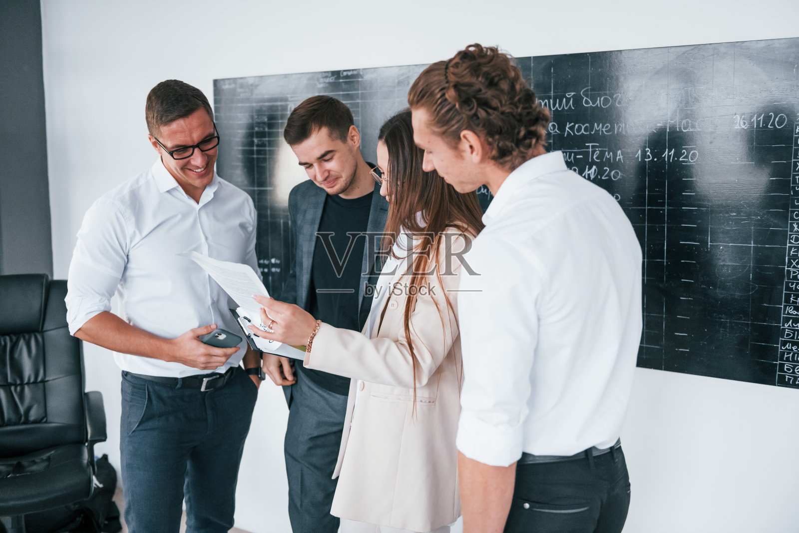 手里拿着文件。一群聪明的年轻人站在办公室的黑板旁边照片摄影图片