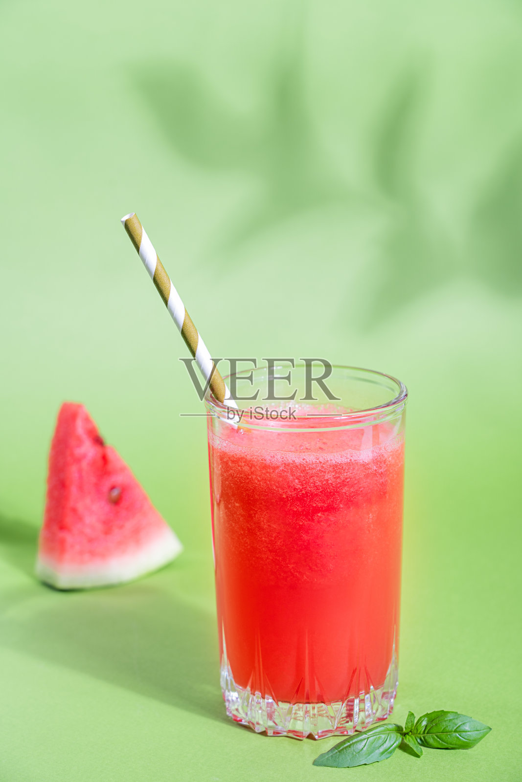一杯清爽的西瓜汁，配上纸吸管和罗勒叶，背景是绿色的植物阴影照片摄影图片