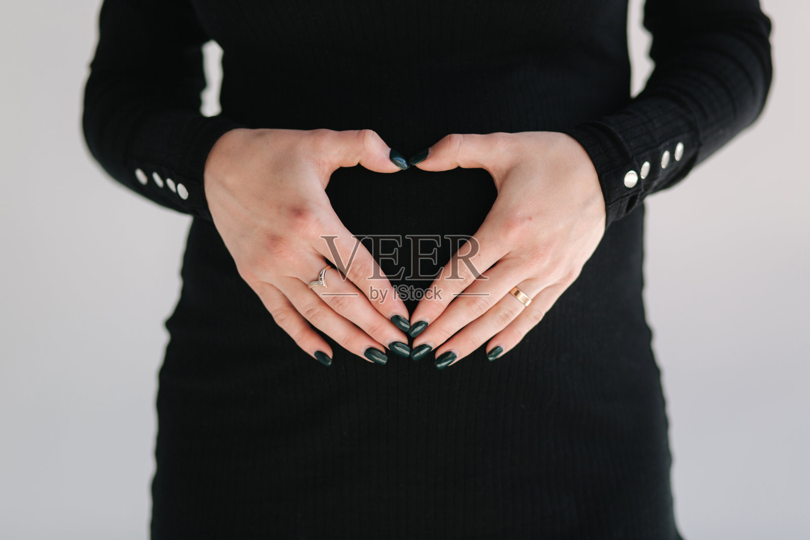 中选孕妇将手放在腹部。穿着黑色紧身连衣裙的女性。白色背景照片摄影图片