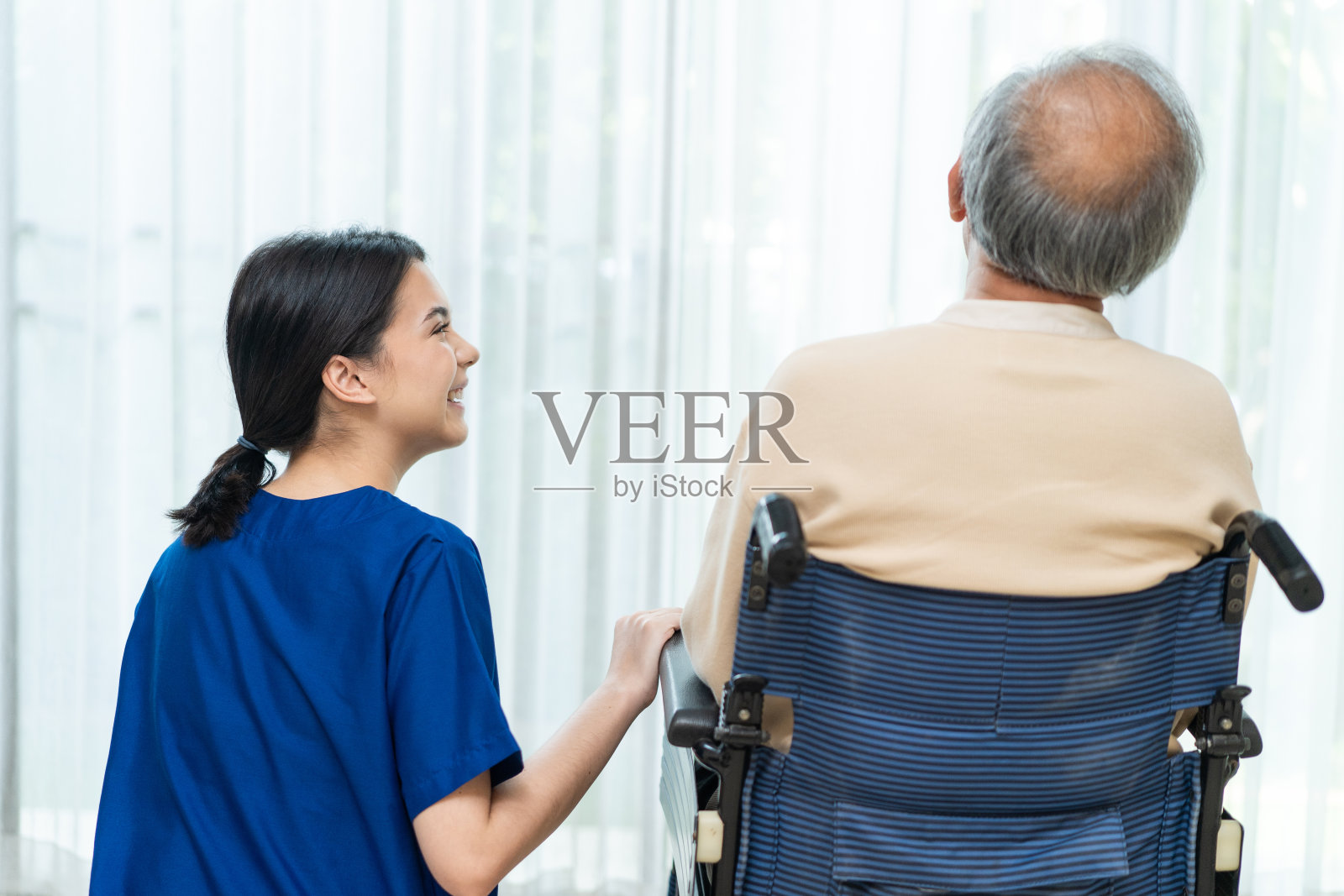 亚洲护士在养老院照顾轮椅上的老人。漂亮快乐的看护者女孩医生问候和交谈的老年老年残疾患者男性在医院病房。照片摄影图片