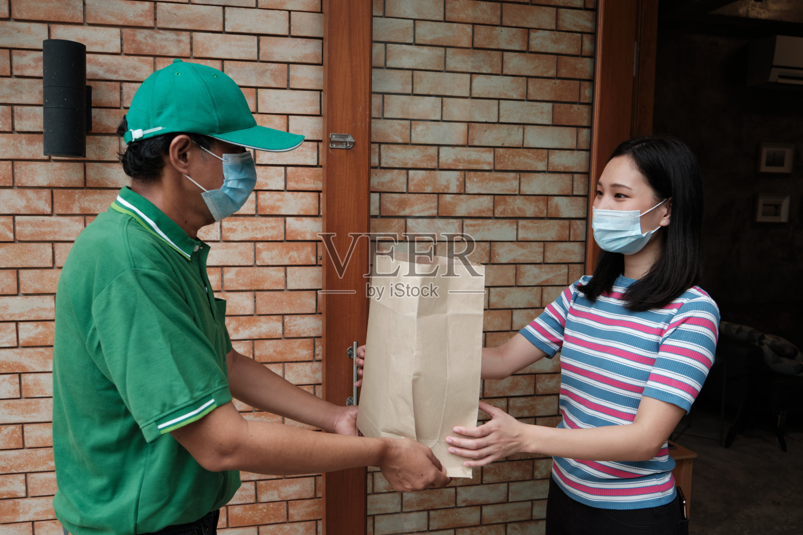 戴口罩的快递员将包裹交给一名亚洲妇女。照片摄影图片