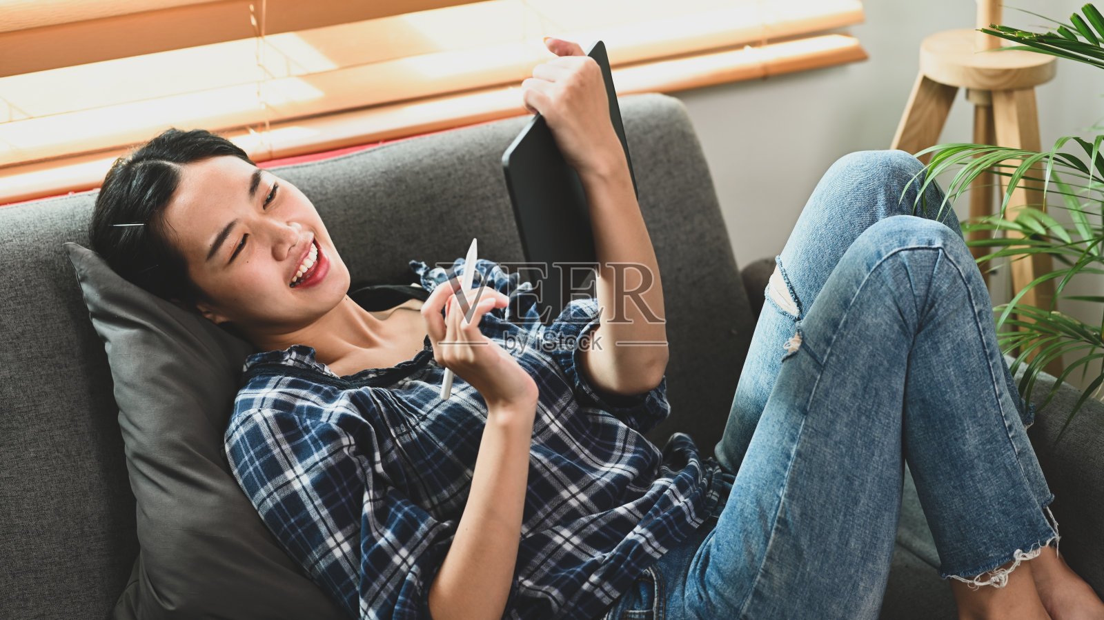 微笑的女人在客厅的沙发上休息和使用数字平板电脑。照片摄影图片